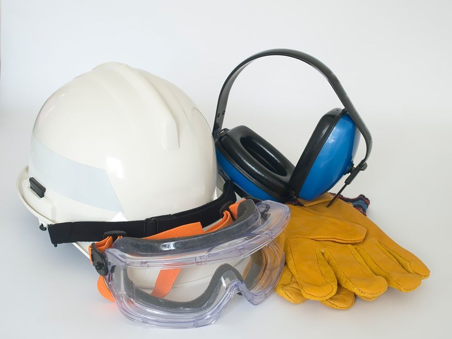 Un casco, orejeras, gafas protectoras y guantes sobre una superficie blanca