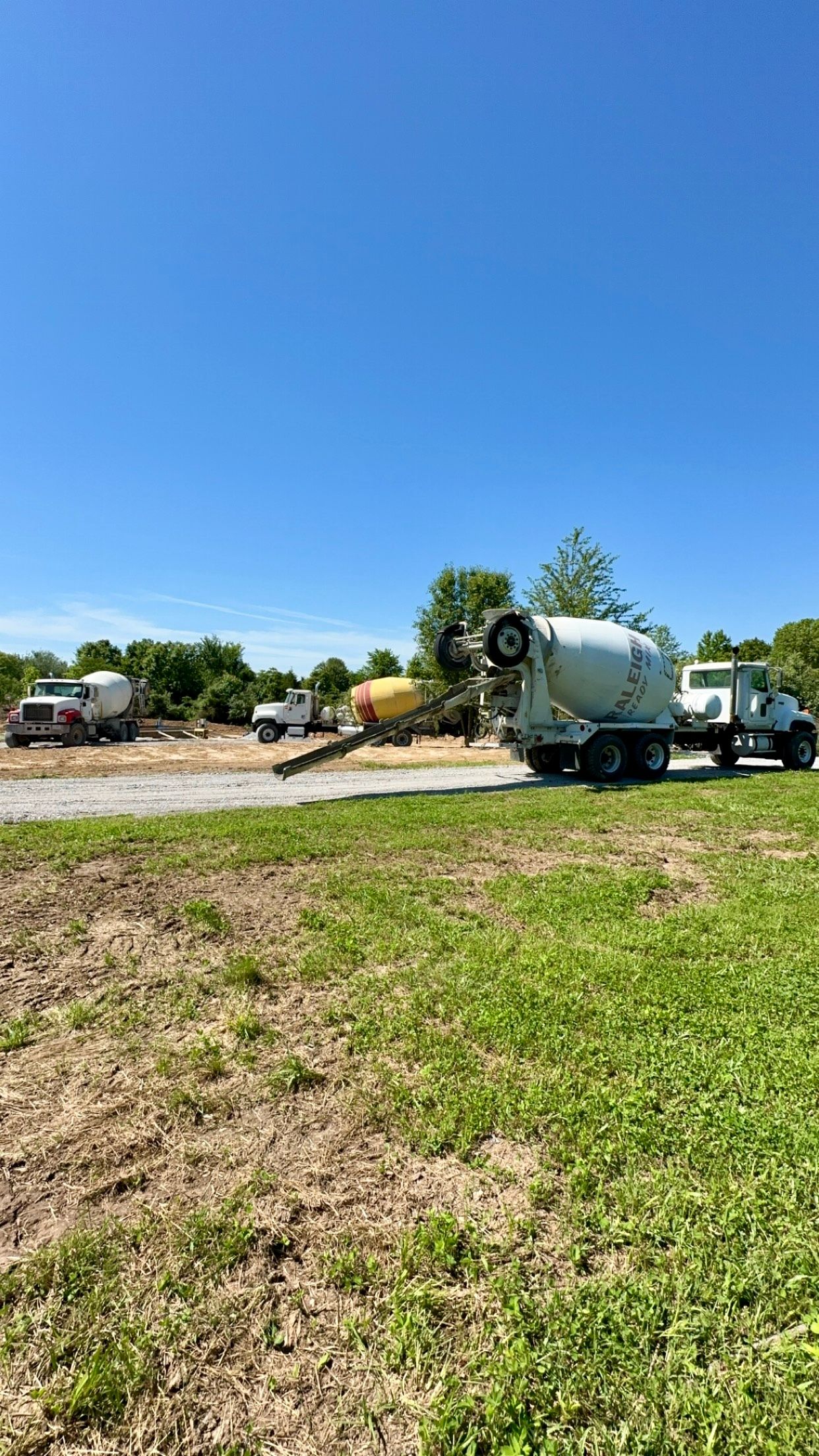 Cement mixer truck parked beside a gravel road under a bright blue sky in a rural field