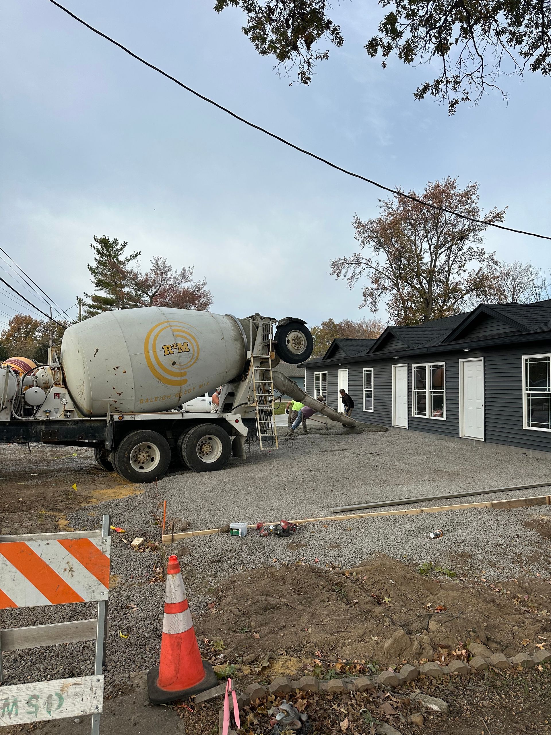 Concrete mixer truck parked beside a dark house with roadwork cones and barricade tape in front