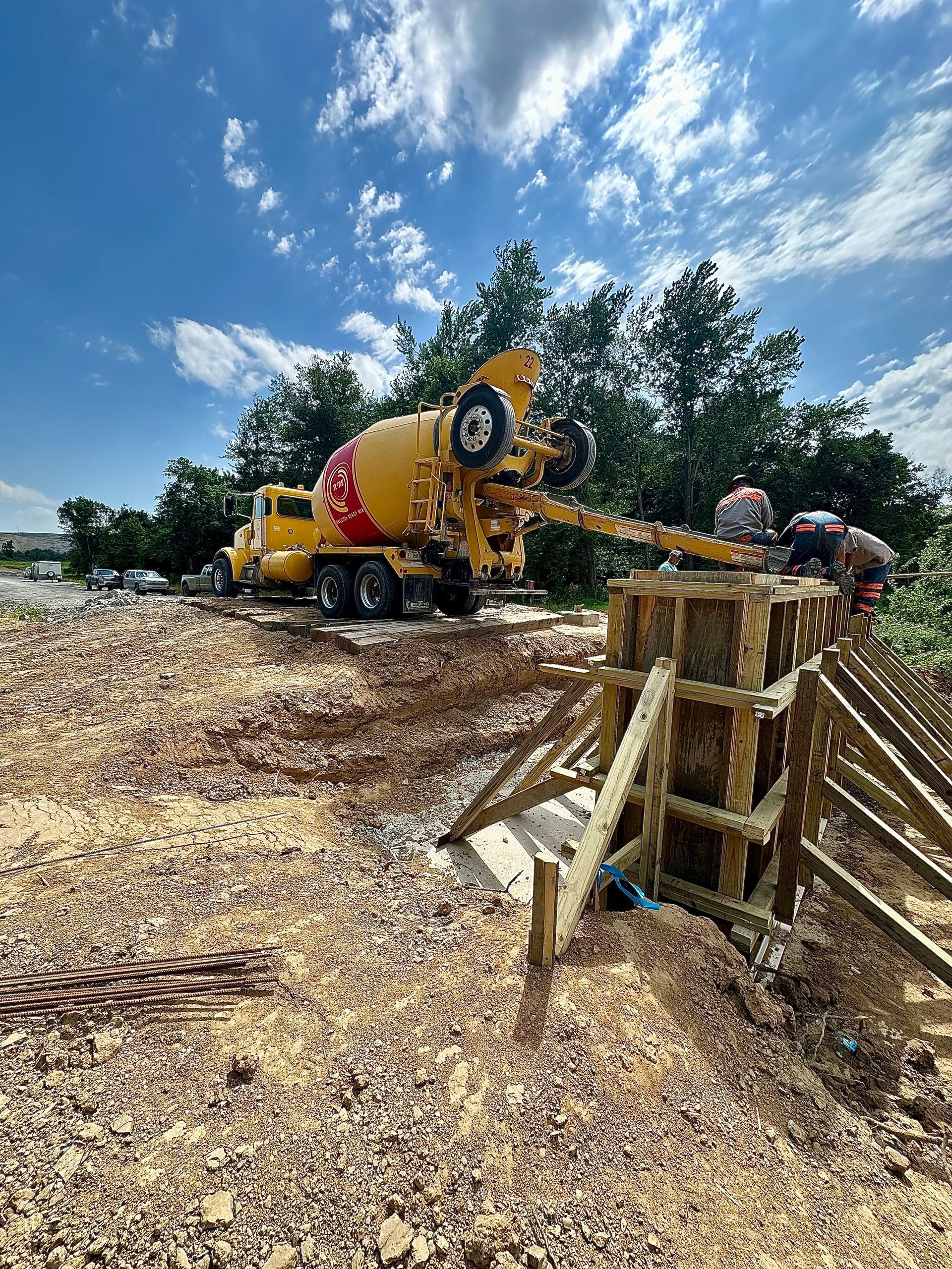 Yellow cement mixer truck at a construction site with wood forms and scattered debris under a blue sky