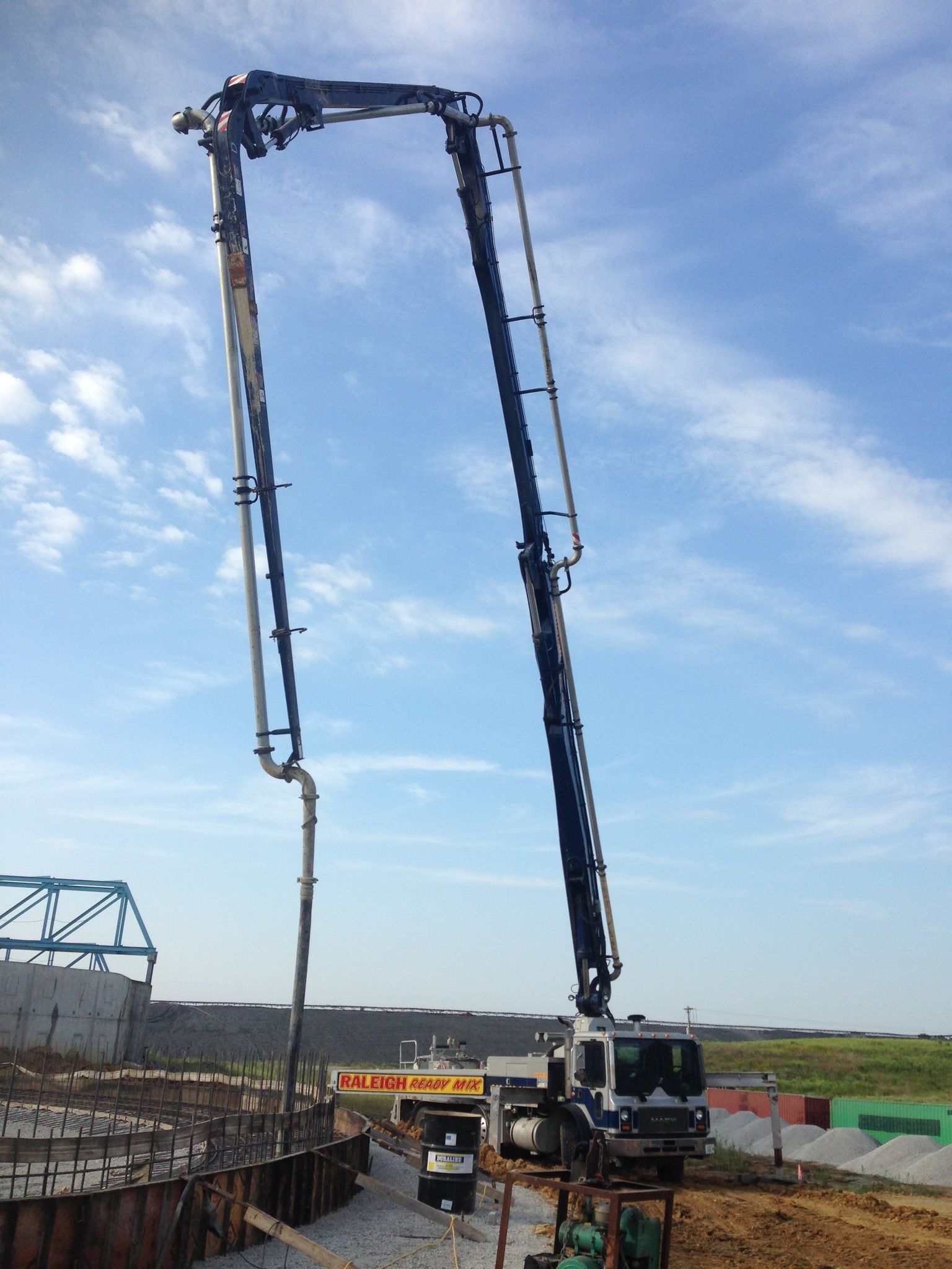 Concrete pump truck with a long black boom pouring concrete at a construction site under a blue sky