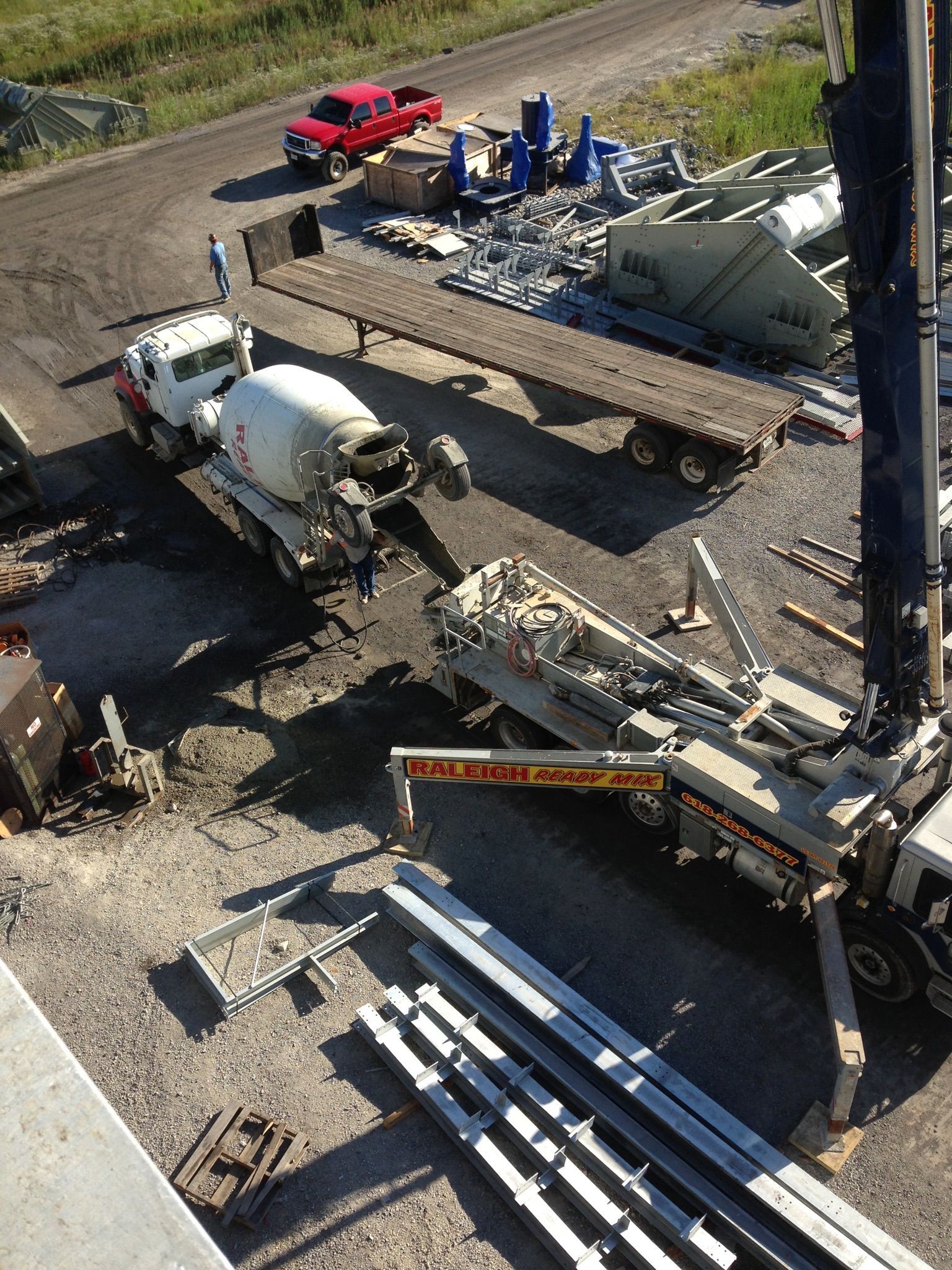 Construction site with concrete truck, crane, and stacked steel pipes