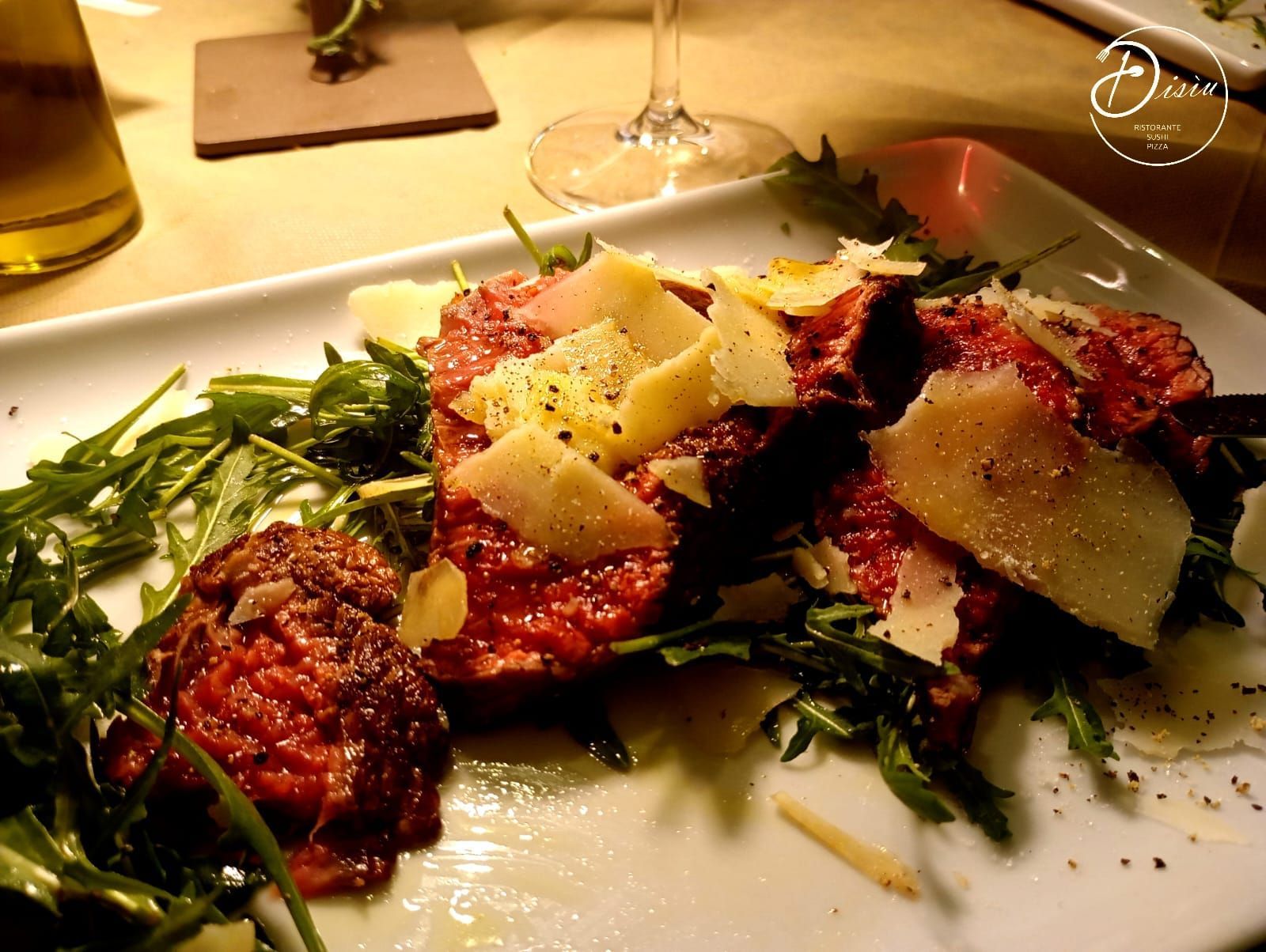 Antipasto di bistecca con rucola, parmigiano e pepe servito su un piatto bianco rettangolare.