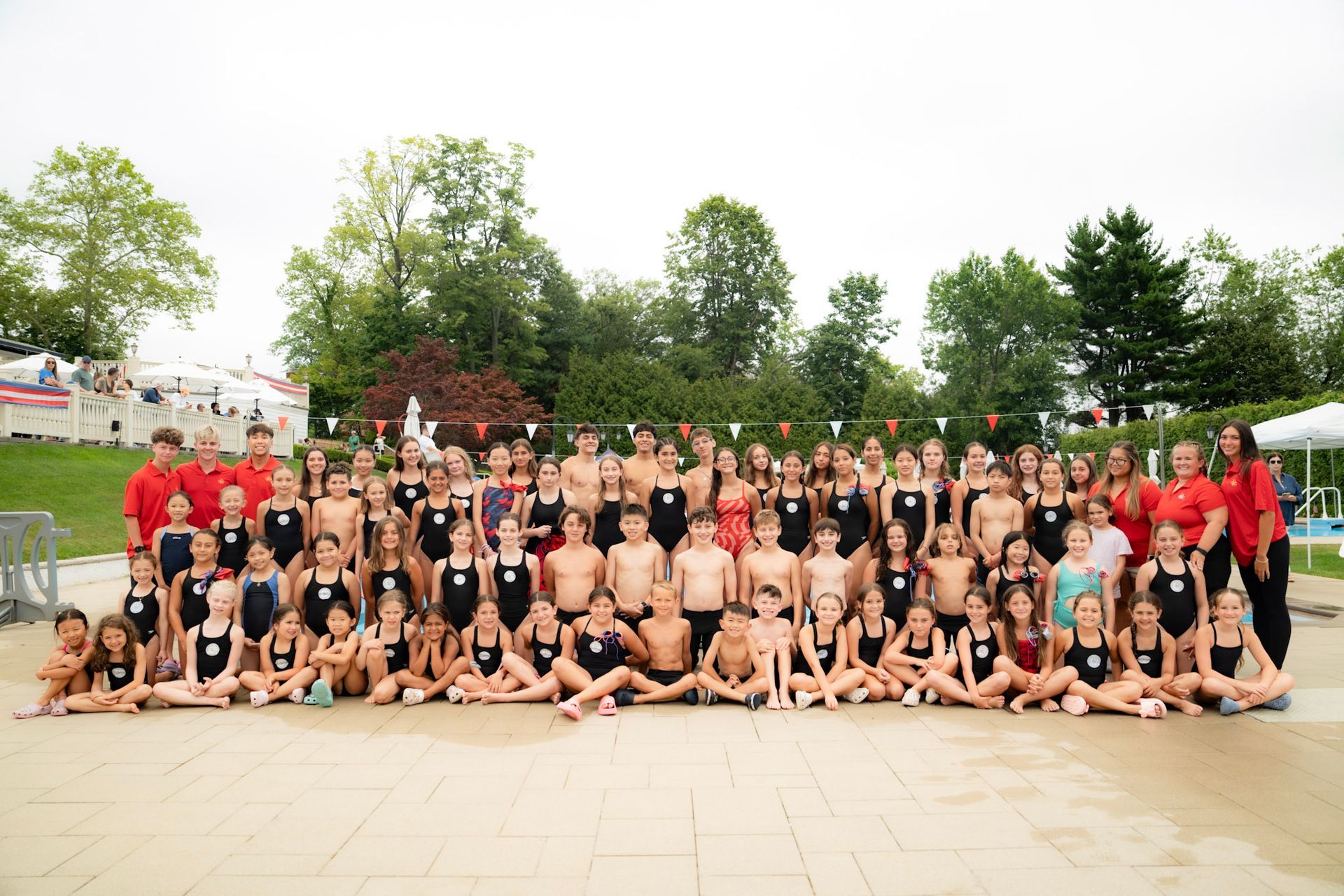 Group of young swimmers posing by a pool, sunny day.