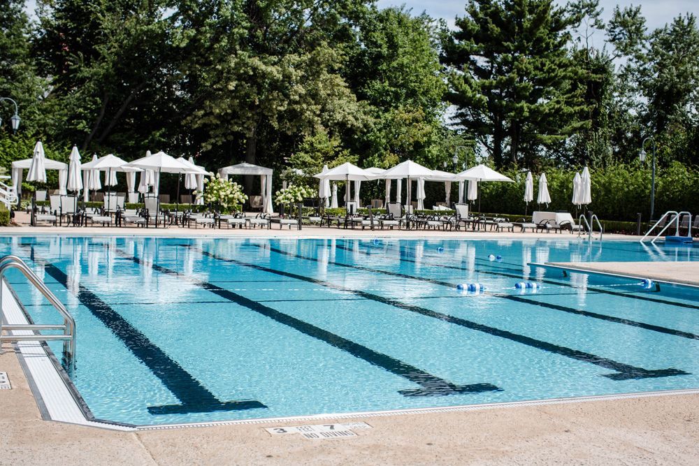 Swimming pool with marked lanes, lounge chairs, and shaded seating area.