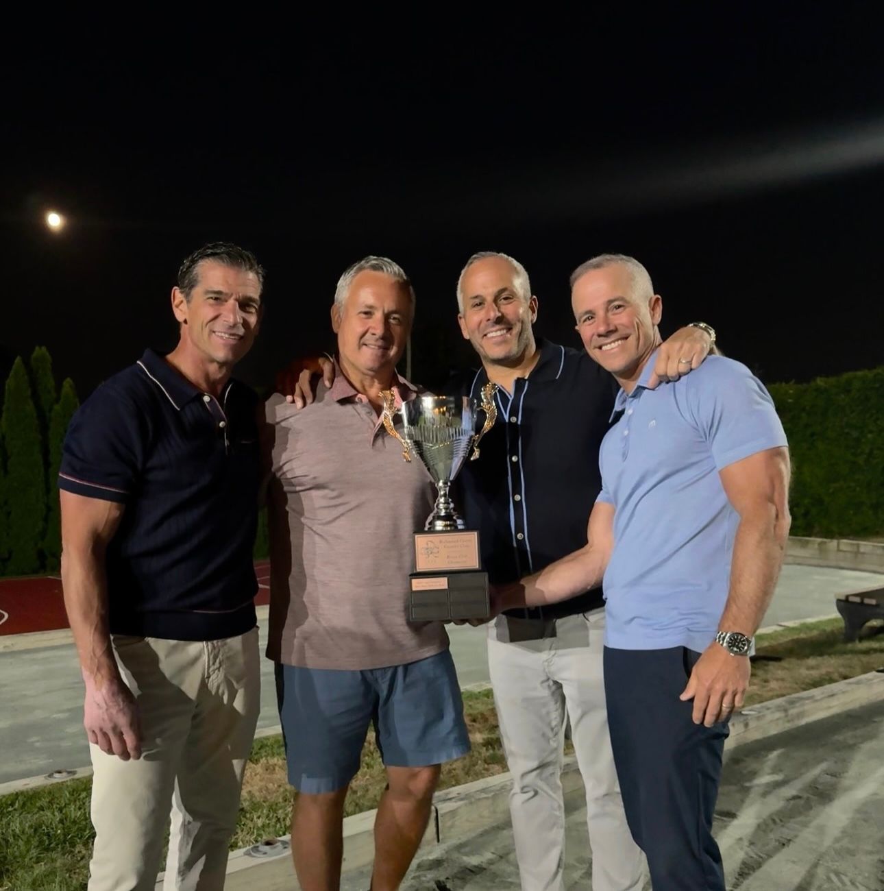 Four men holding a trophy outside at night, celebrating a win.