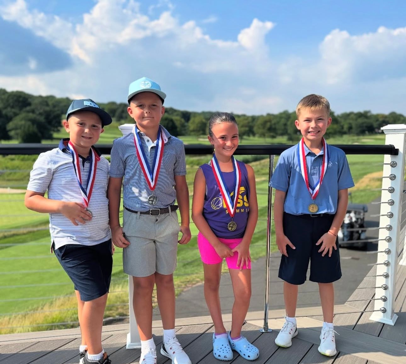 Four young golfers with medals pose on a deck overlooking a golf course.