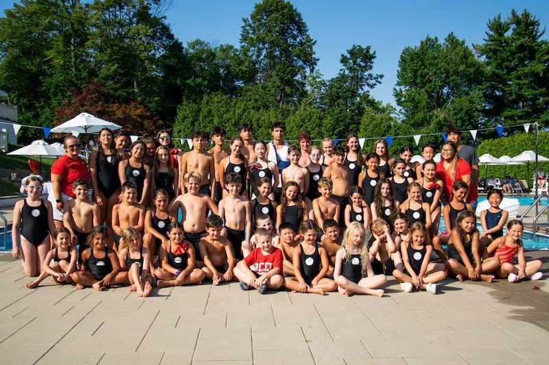 Group of young swimmers posing by a pool, sunny day.