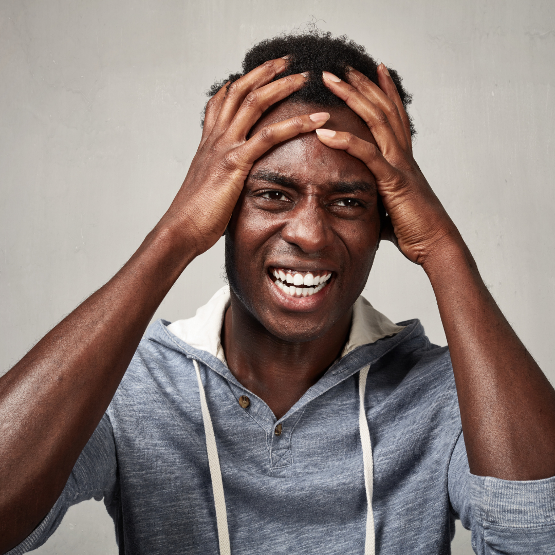 Man with dark skin, hands on head, distressed expression, wearing a gray hoodie.