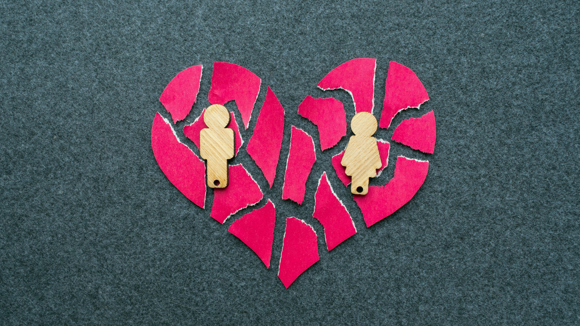 A broken red heart with silver edges and wooden male and female figures, symbolizing a breakup.