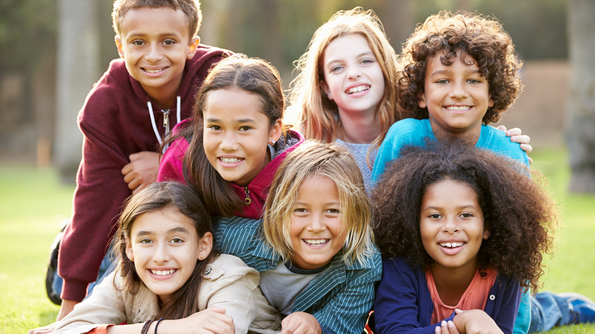 Group of diverse children smiling, posing on grass. Outdoors.