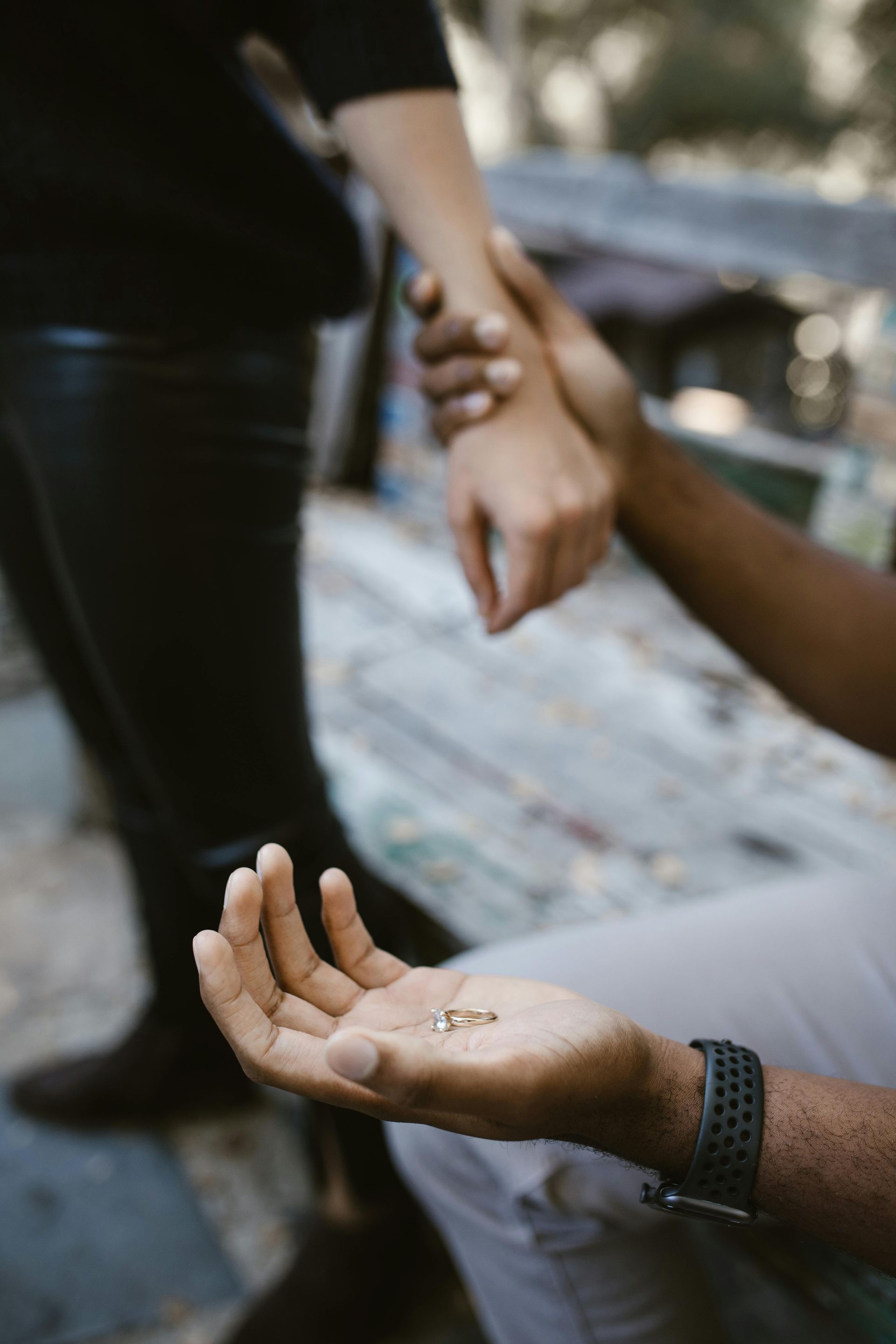 Man holds small objects in his open palm while holding the other person’s wrist. They are outdoors.