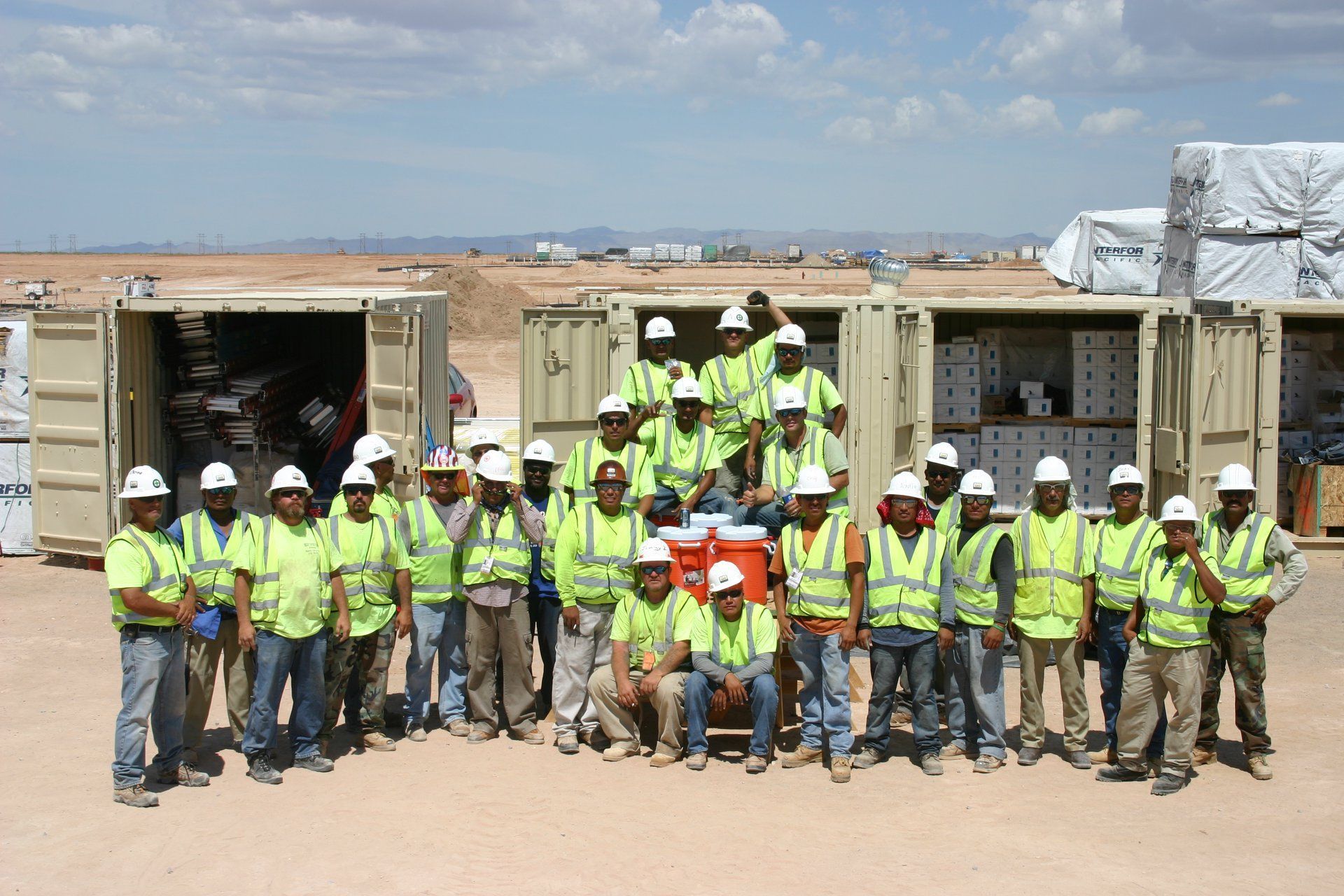 Group of construction workers in neon safety vests and hard hats posing in front of a building site