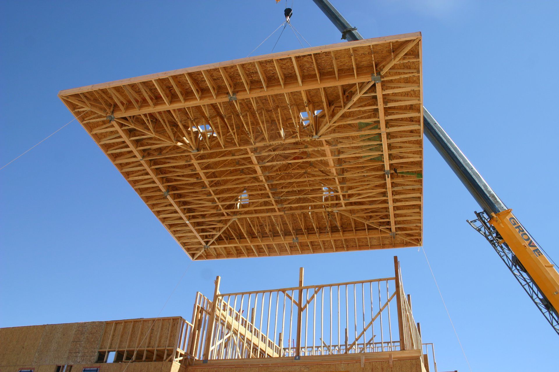 Wooden building panel being lifted by a crane at a construction site against a blue sky