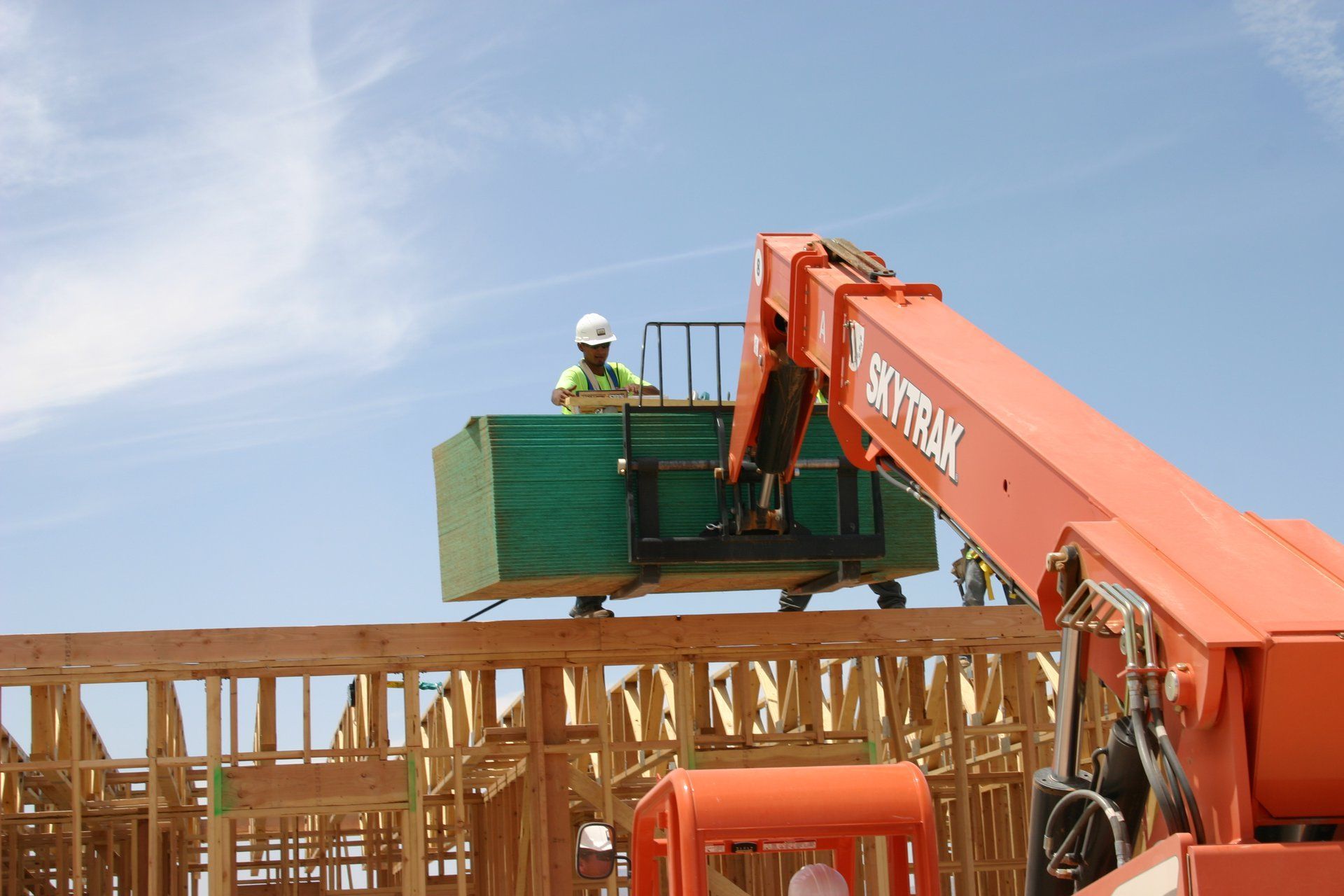 Worker on a telescopic lift placing a green panel atop a wooden structure at a construction site