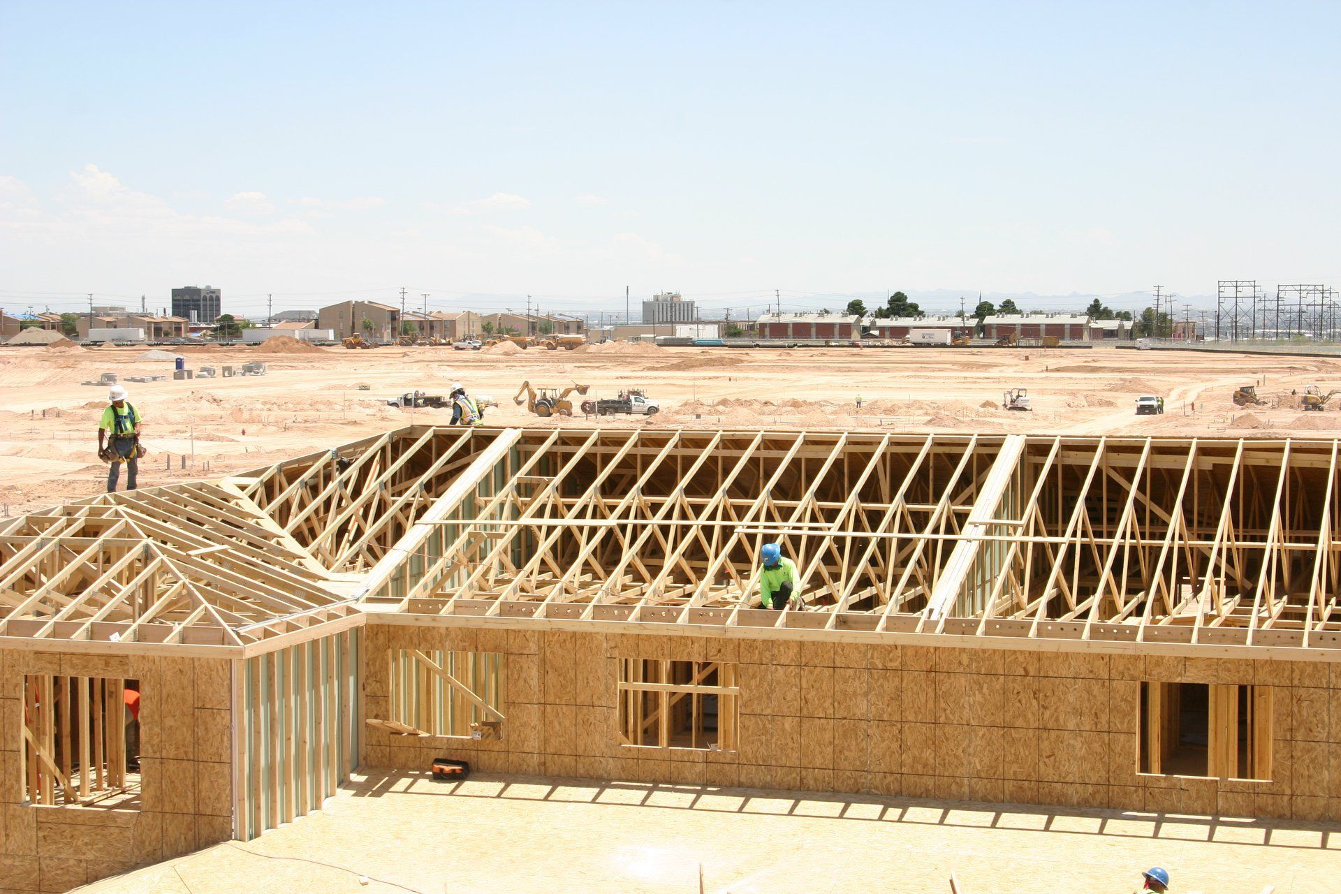 Construction site with wooden house framing and workers in hard hats under a bright sky