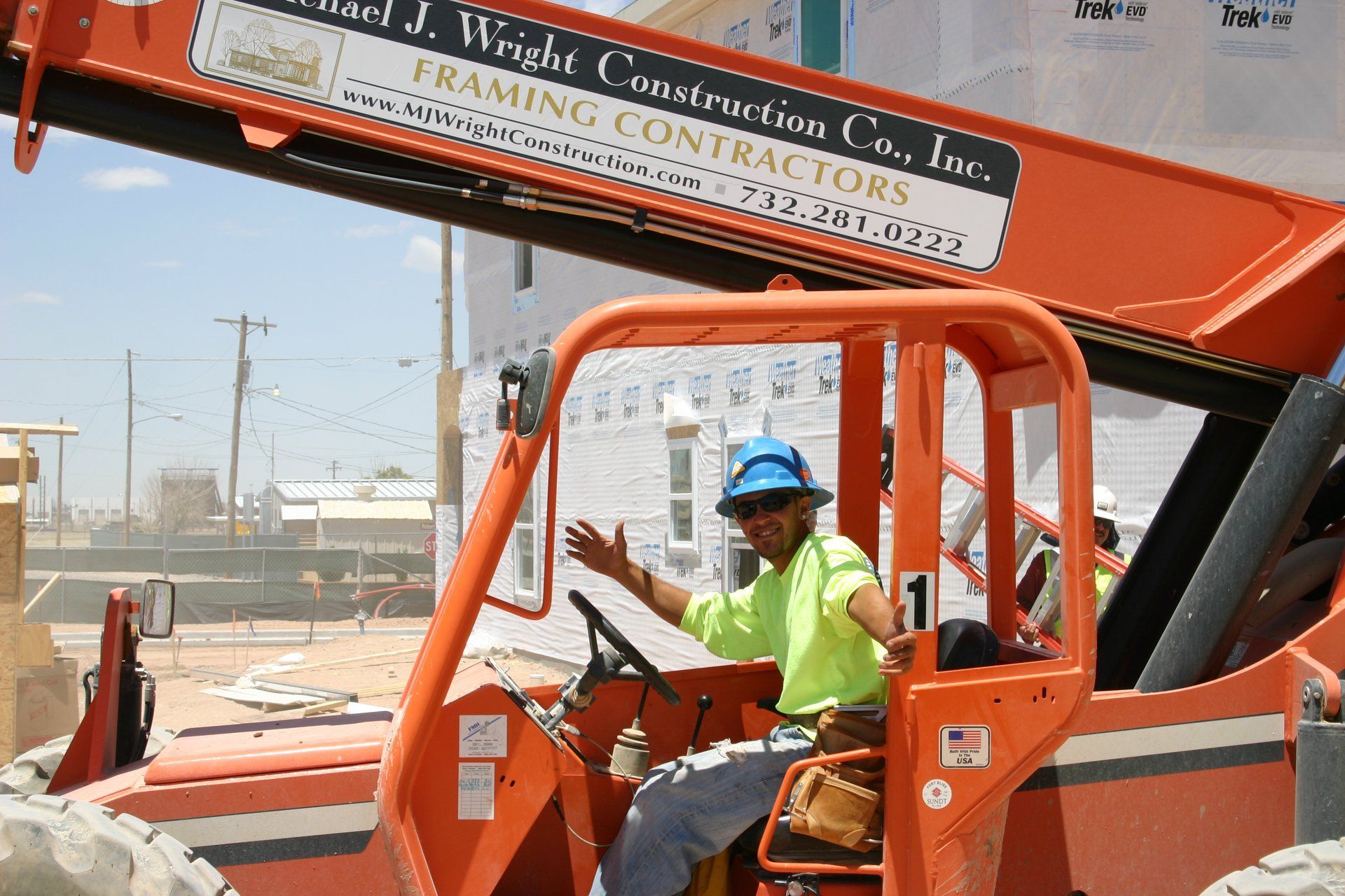 Worker in blue hard hat driving an orange construction lift on a worksite