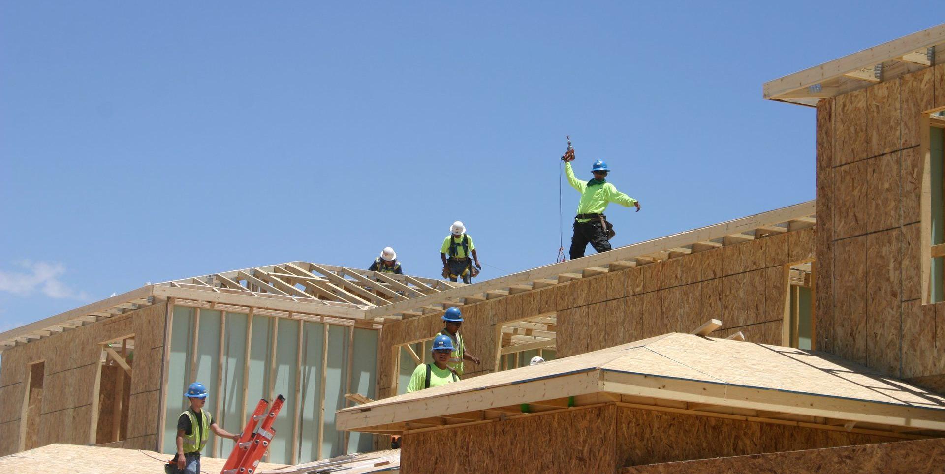 Workers in safety vests and helmets on a roof under construction against a blue sky
