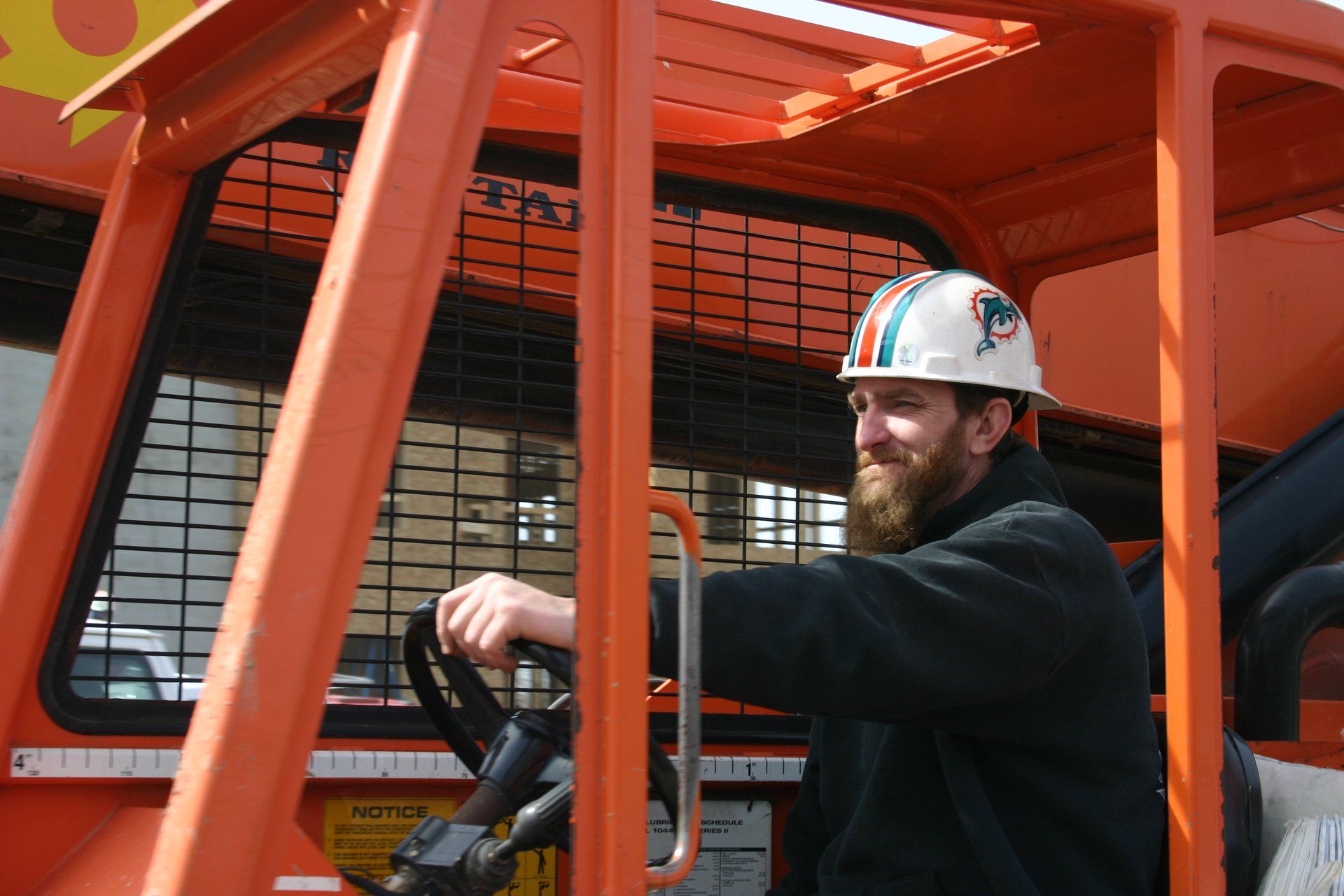 Worker in white hard hat operating machinery inside an orange construction vehicle