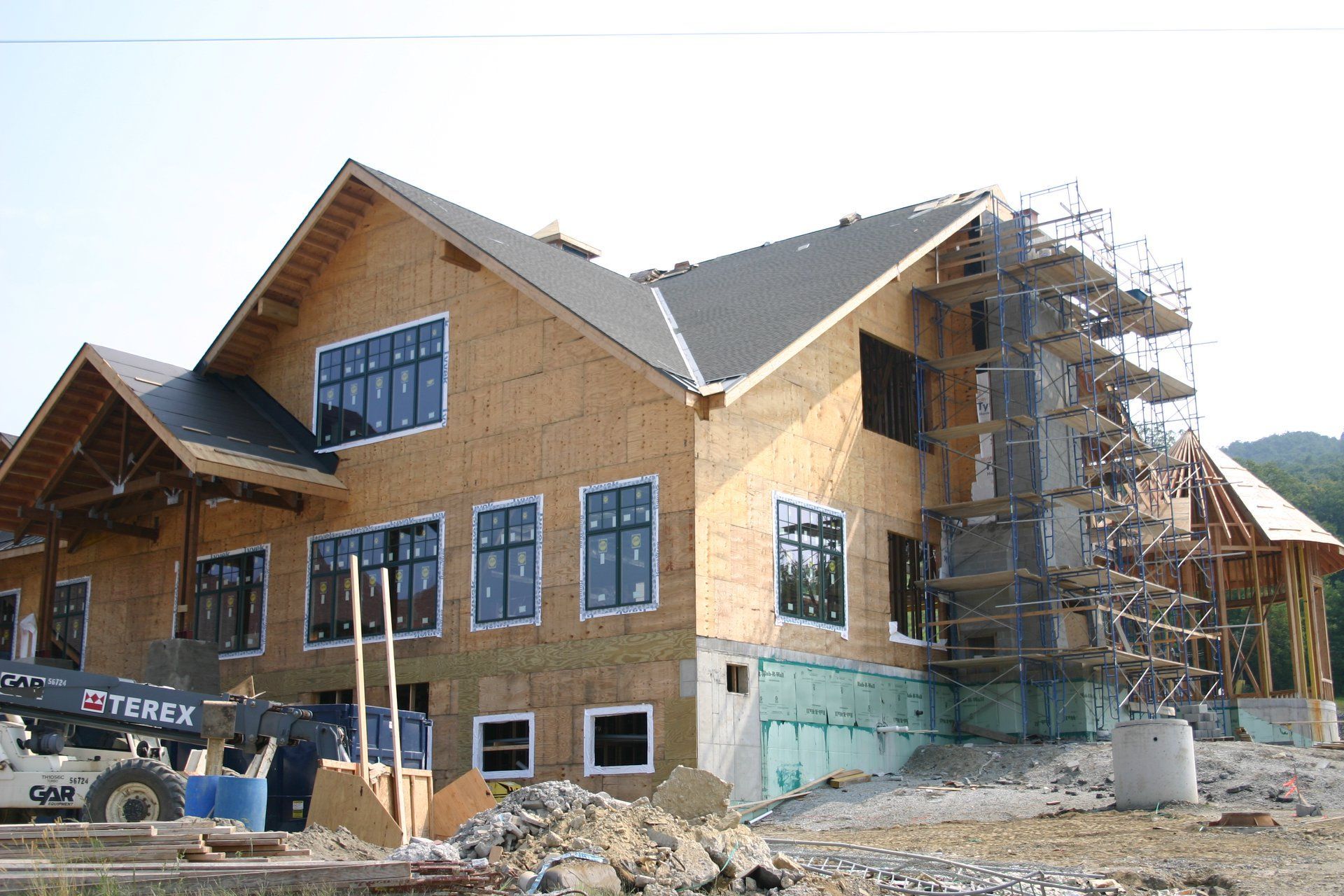 Partially built house with wood siding, blue-trimmed windows, and scaffolding at a construction site
