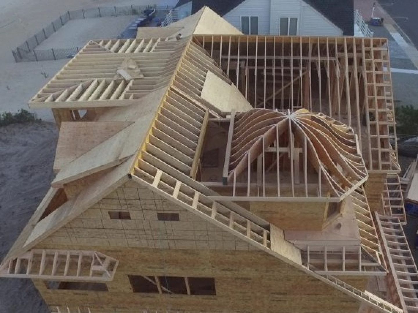 Wooden house under construction with exposed roof framing and a rooftop deck