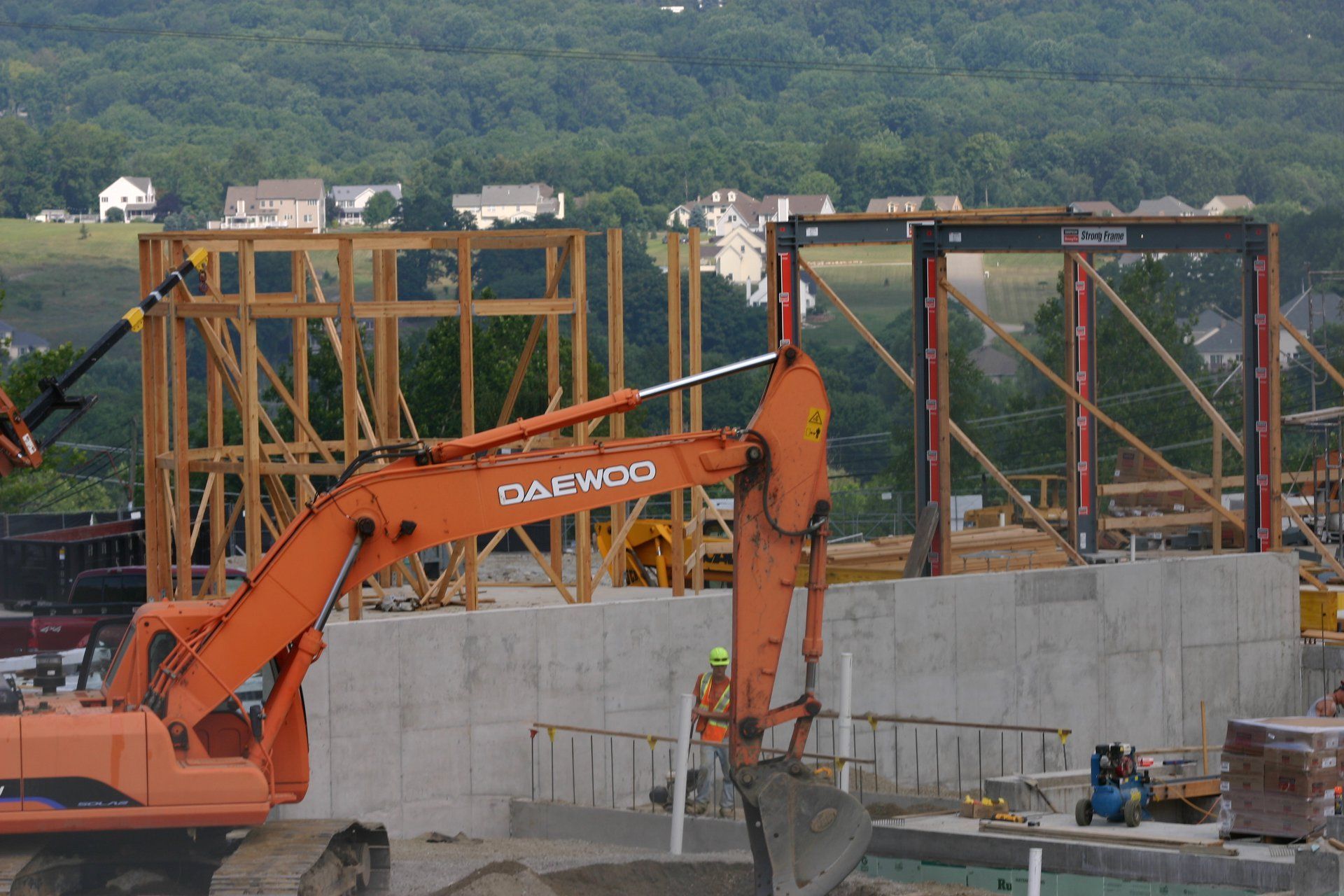 Orange excavator working at a construction site beside a concrete wall and steel frame structure