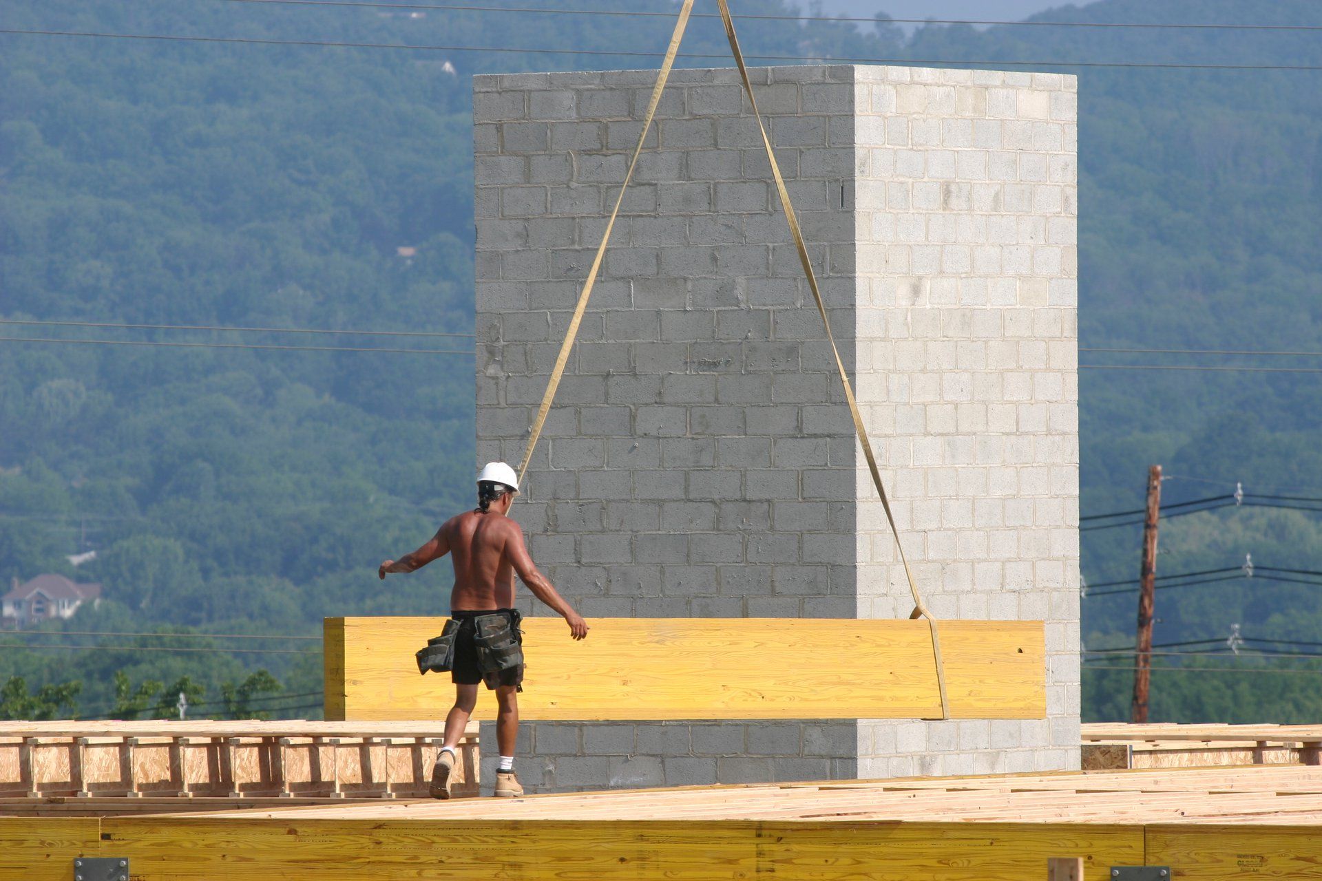 Construction worker on a suspended platform beside a concrete wall, with mountains in the background