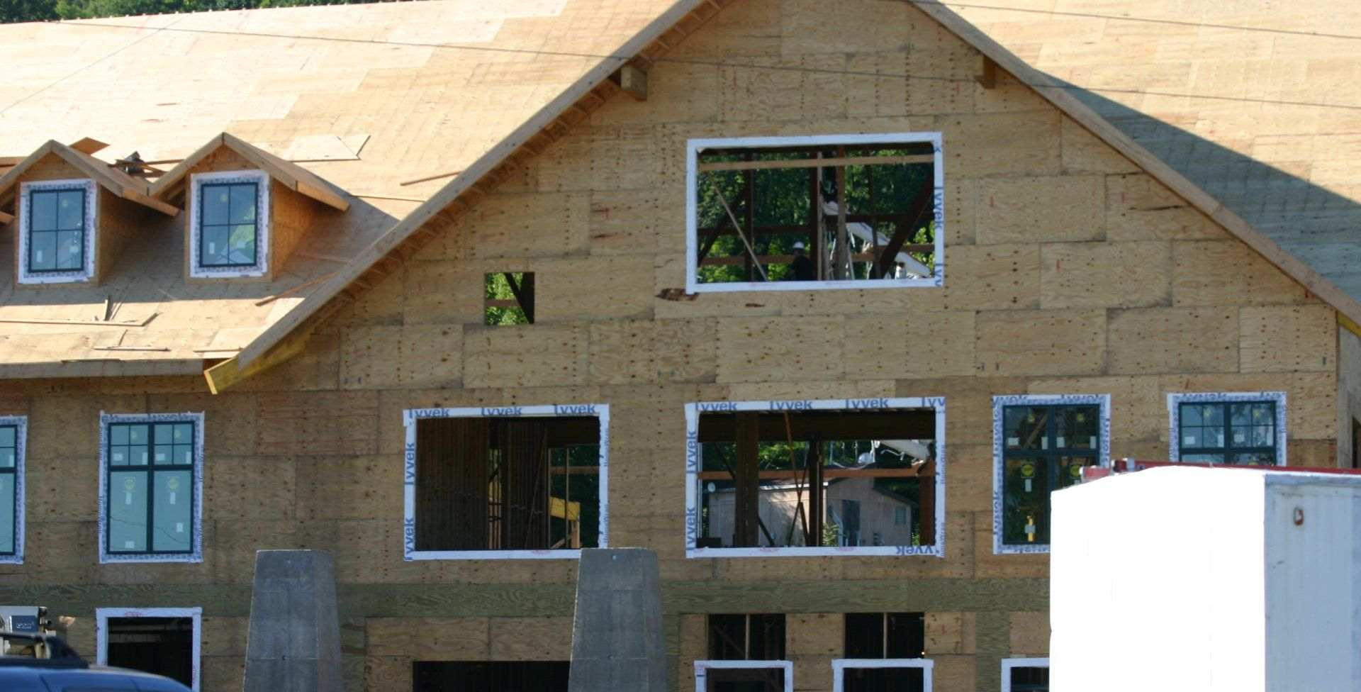 Partially built house with tan siding, dark roof, and window openings against a clear sky