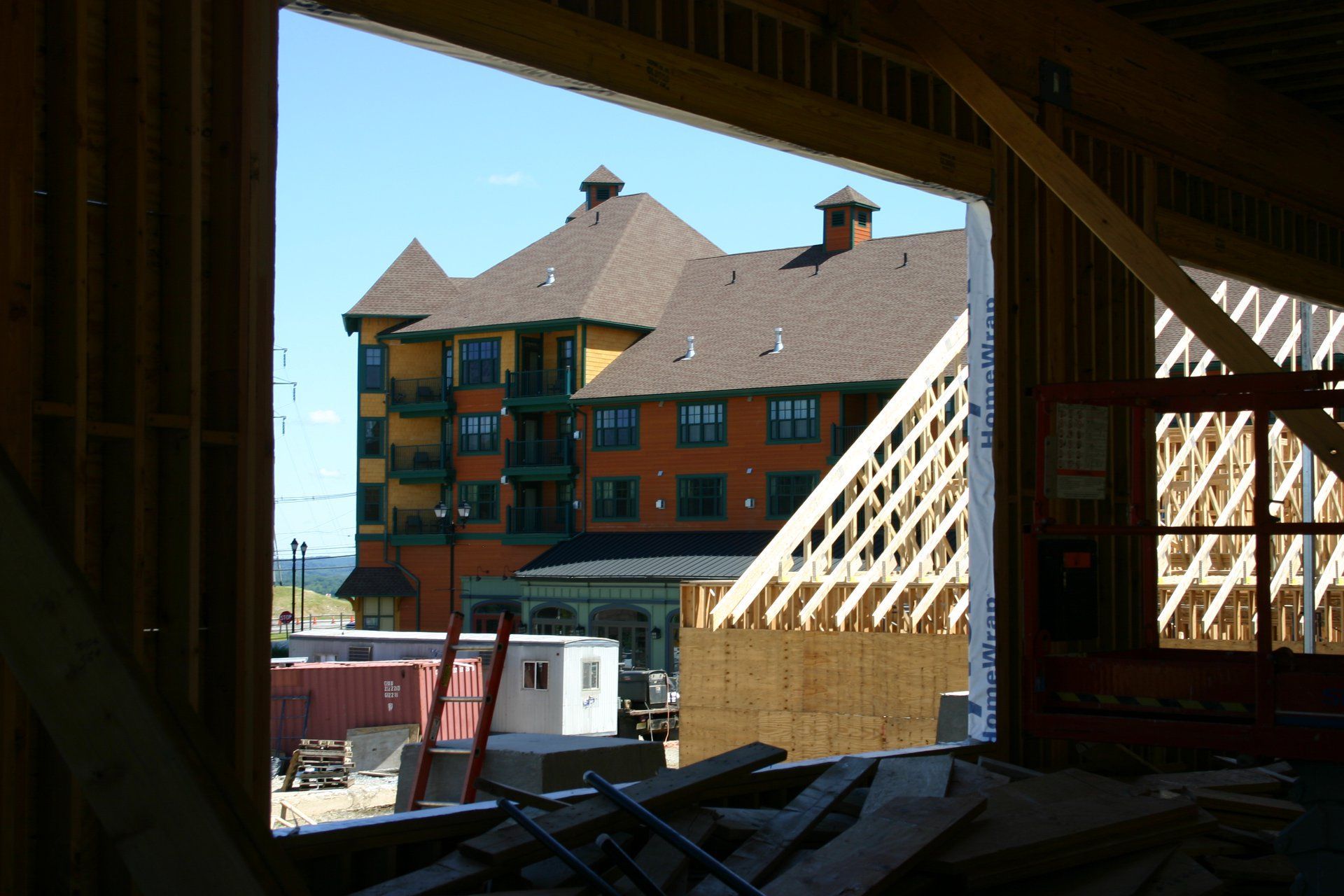 View through a dark wooden frame to a colorful building under construction, with wooden beams in the foreground