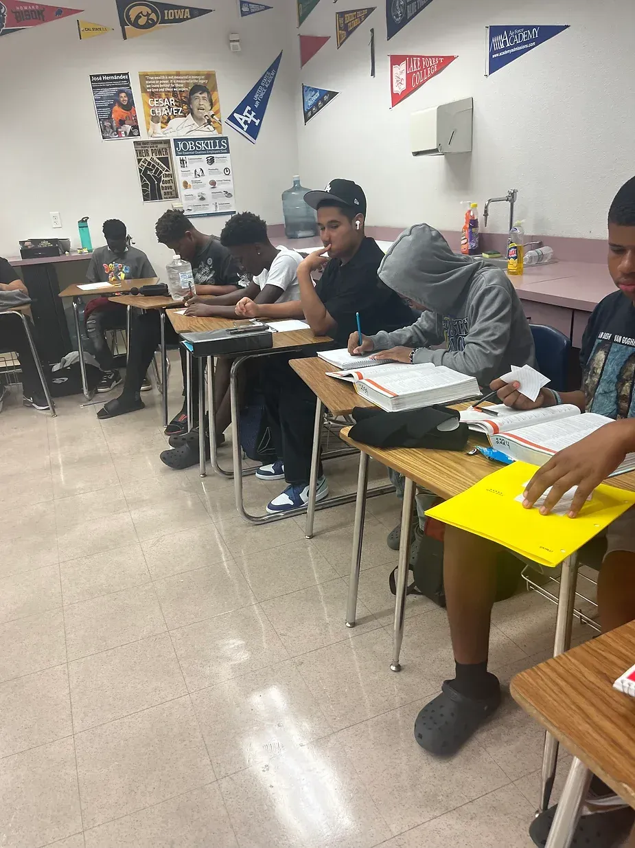 A group of young men are sitting at desks in a classroom.