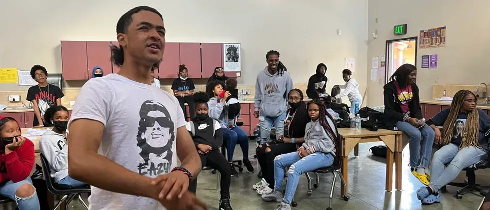 A man is standing in front of a group of people in a room.