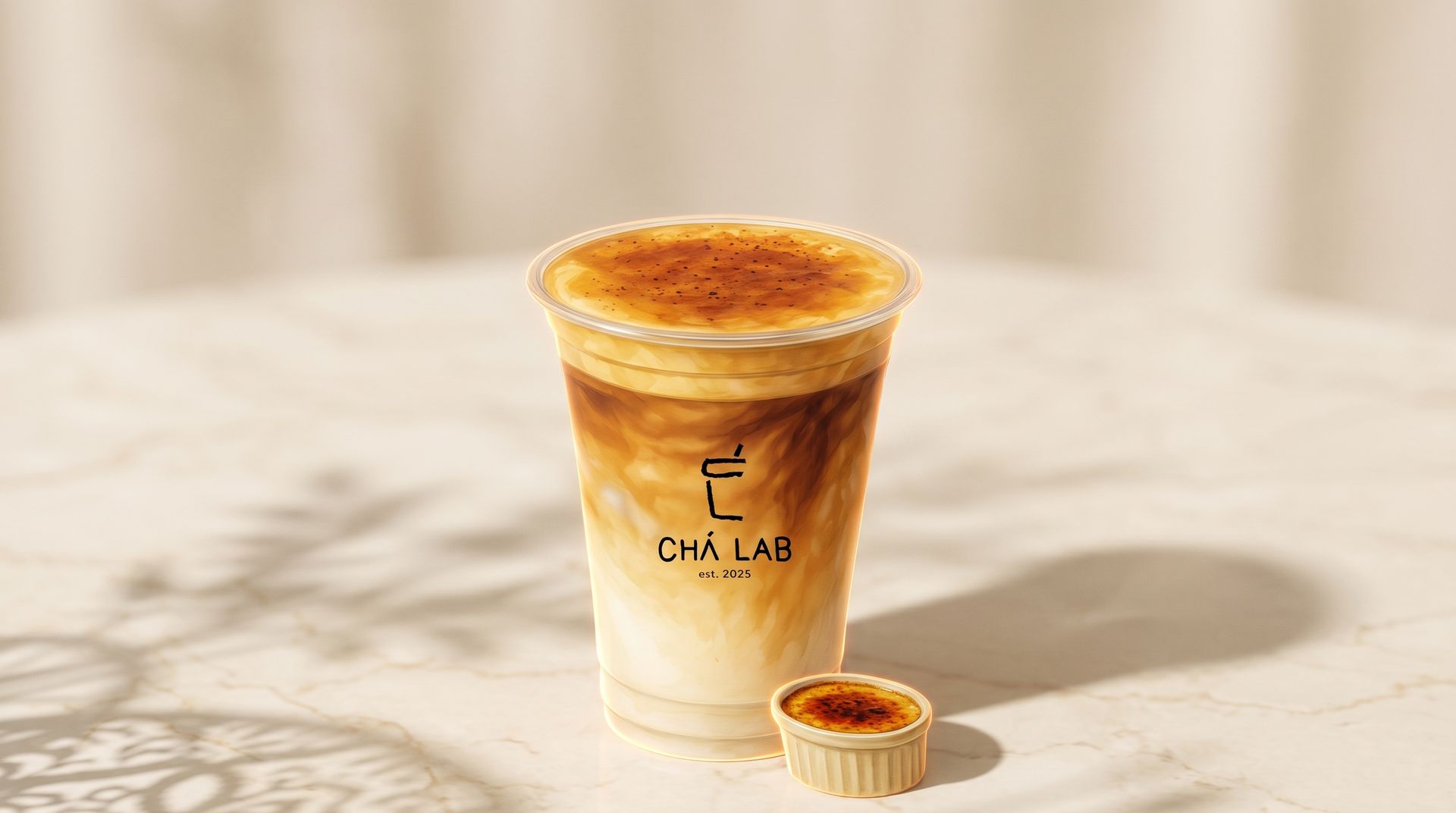 Iced coffee in a clear plastic cup with logo, topped with foam on a marble surface, with a small dessert beside it