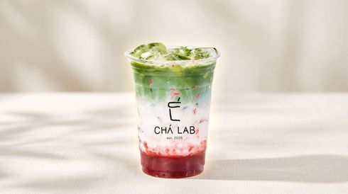 Clear plastic cup with red drink, ice, and green mint garnish on a light table