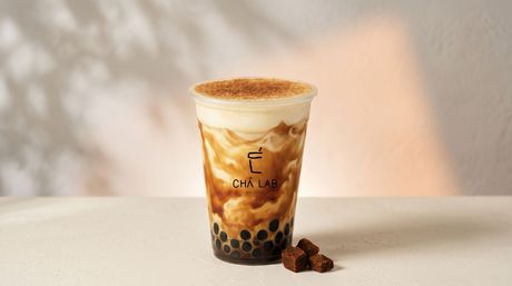 Iced bubble tea in a clear cup with black tapioca pearls on a light table.