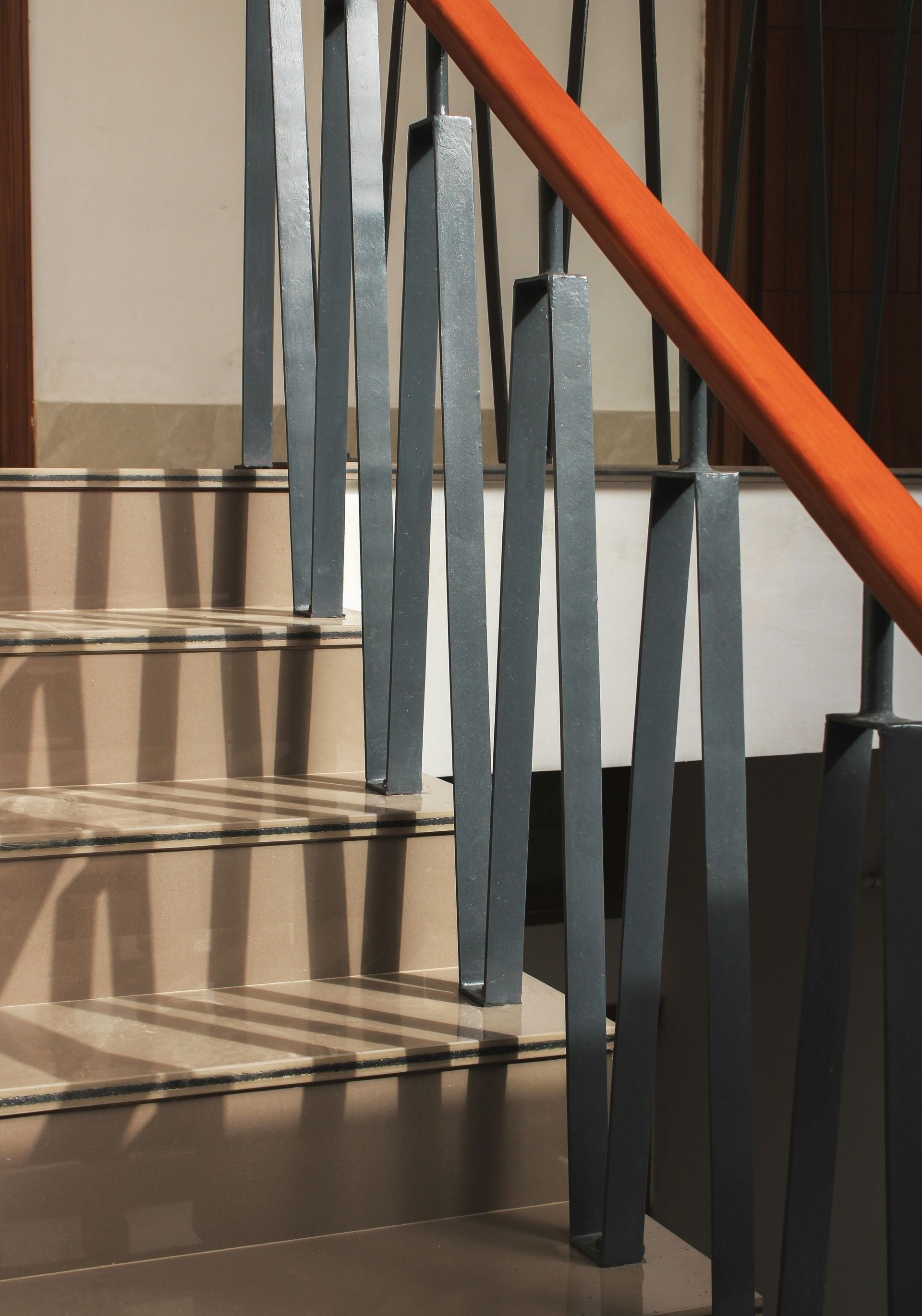 Black metal stair railing with orange handrail beside tiled steps outdoors