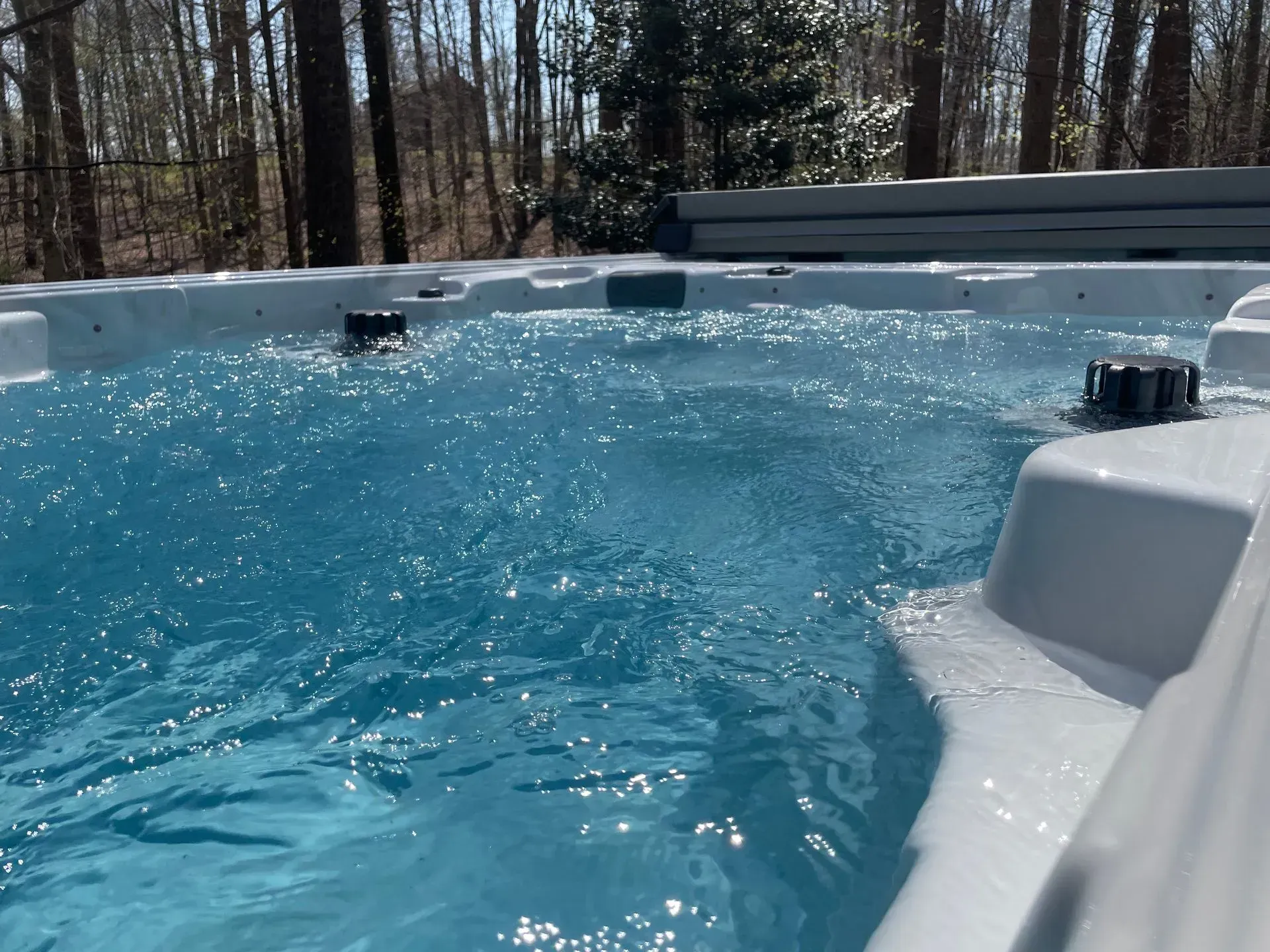 Clear blue water bubbling in a spacious outdoor spa with jets, surrounded by trees.