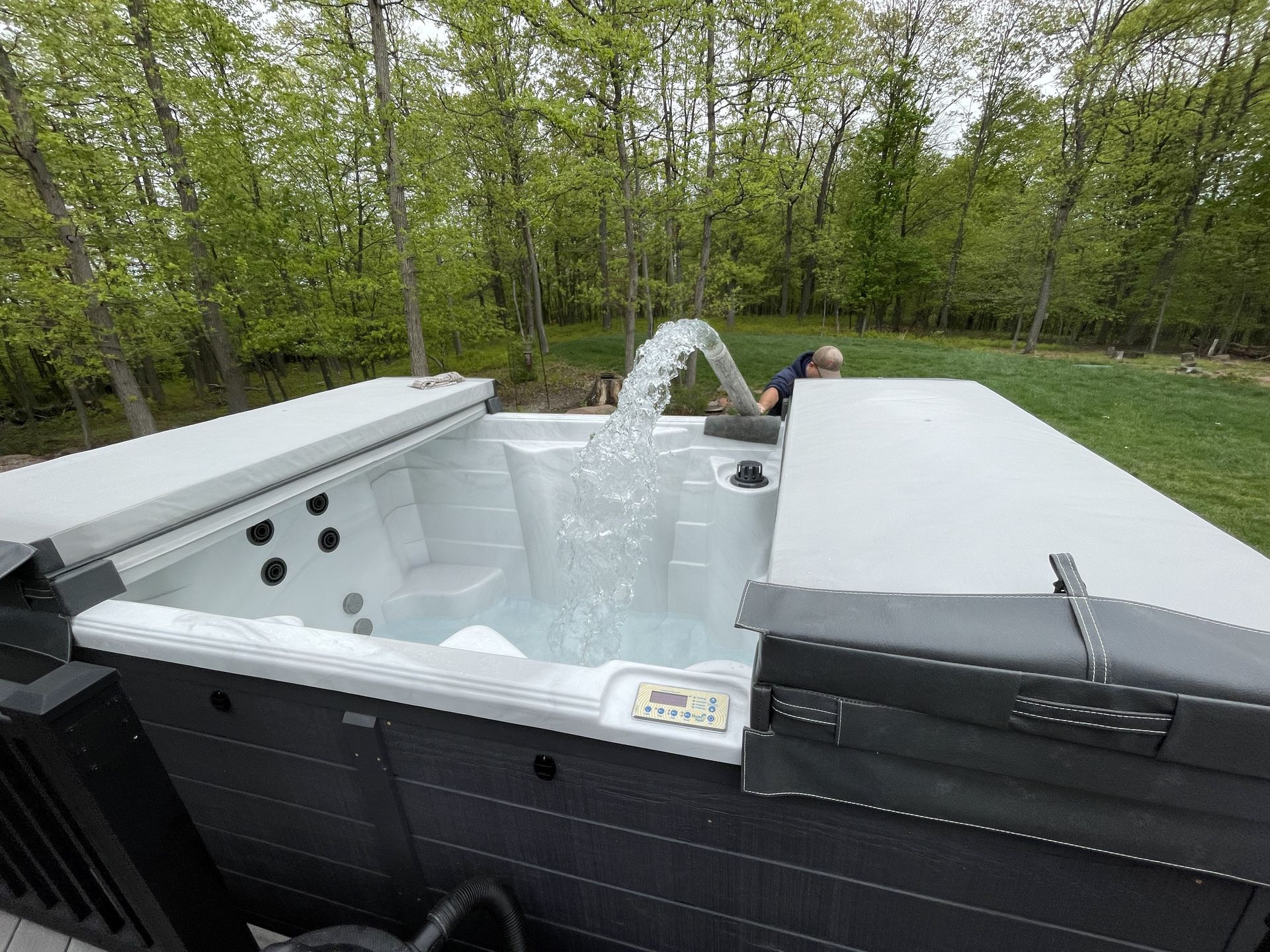An outdoor hot tub with water filled and cover partially open on a concrete patio