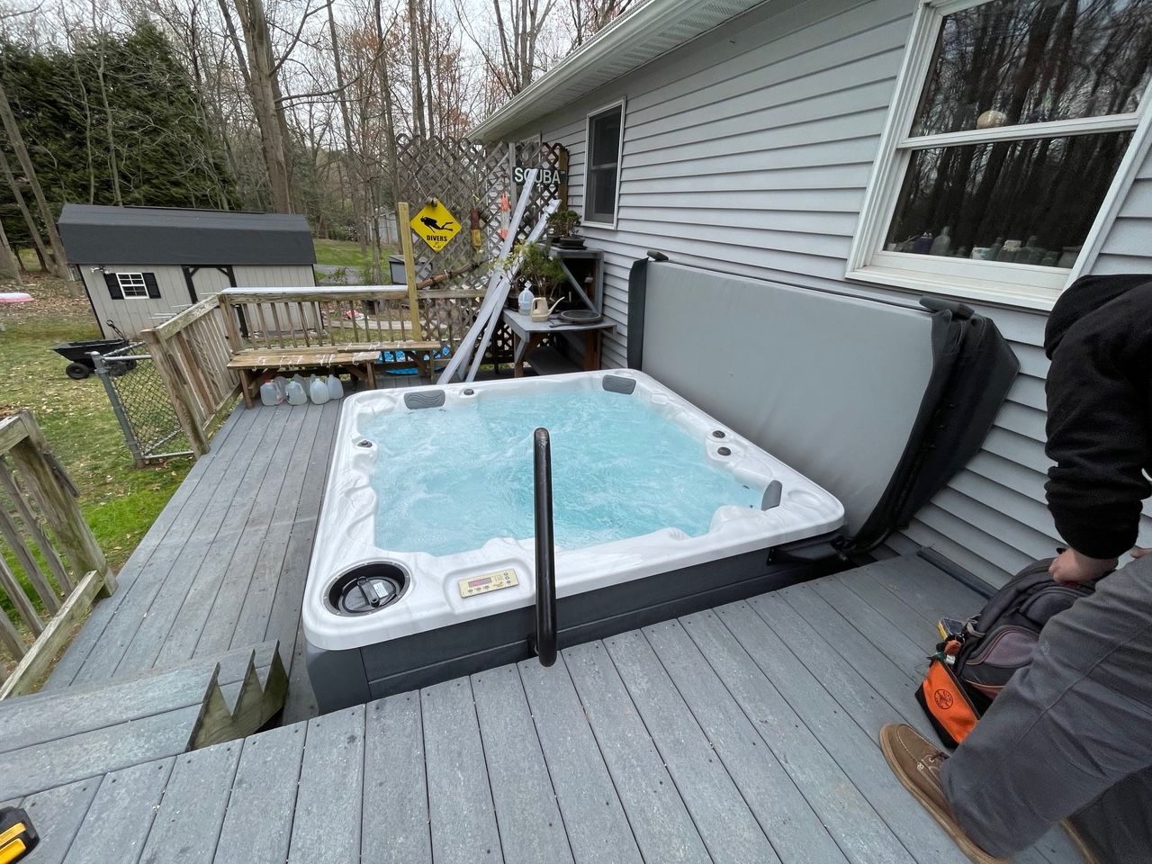 Hot tub on deck next to a house. Man in work clothes near the hot tub.