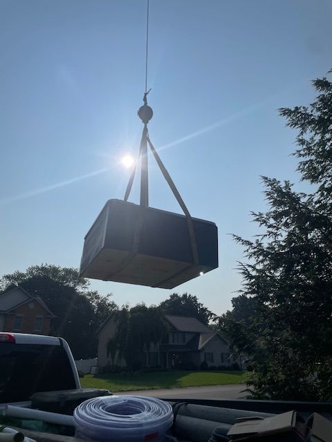 A hot tub is lifted by a crane into a yard with a clear blue sky.