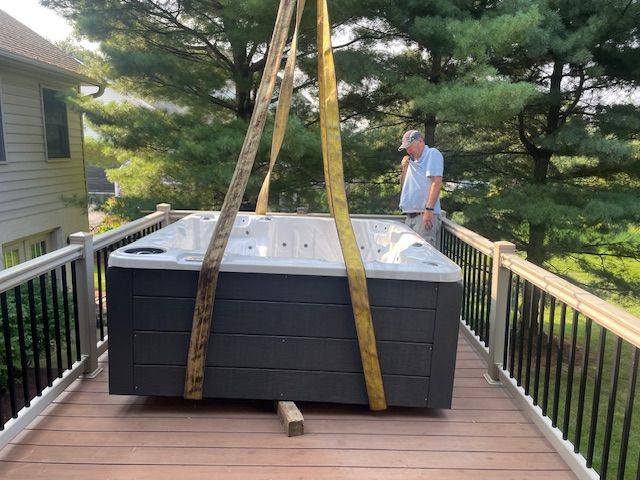 A hot tub being lifted by straps onto a wooden deck; a man watches.