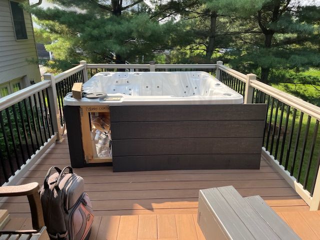 Hot tub on a wooden deck with black railing and brown siding.