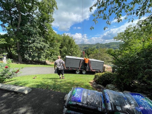 Two men loading panels onto a trailer outdoors, sunny day. Bags of materials in foreground.