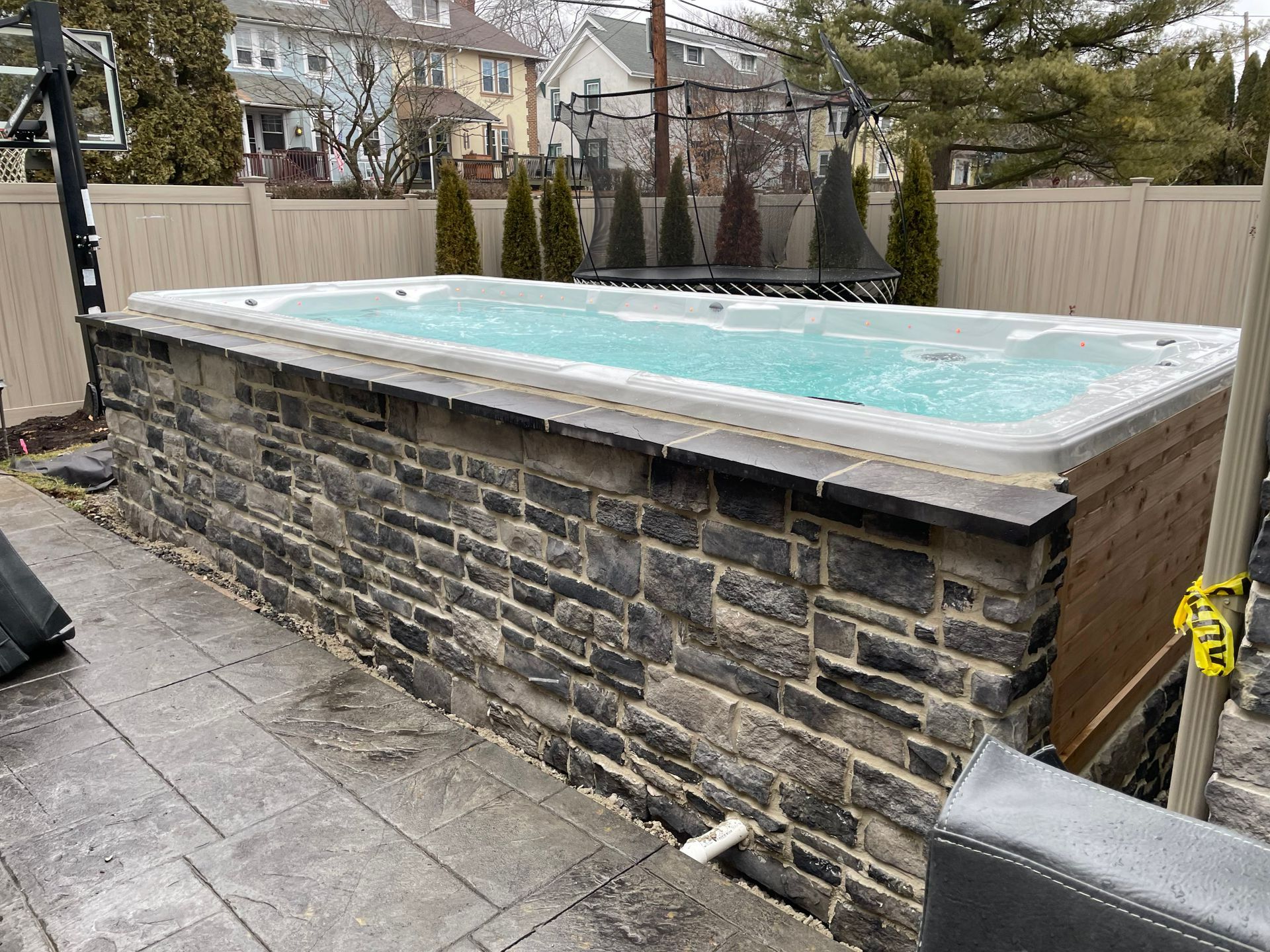 Hot tub with faux stone siding and wooden side paneling in a backyard setting.