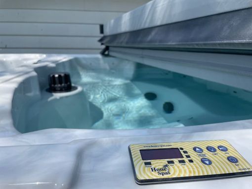 Hot tub with control panel and partially open cover, outdoors.