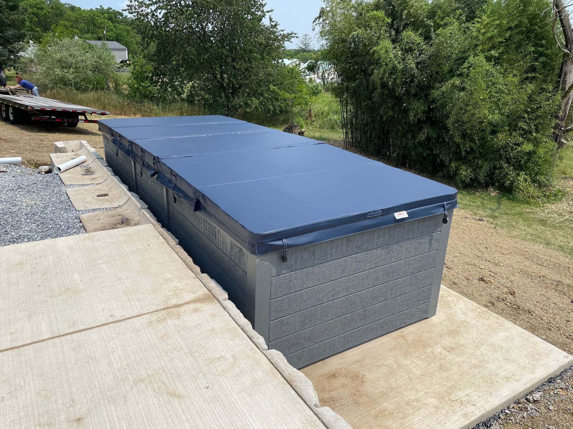 Swim spa with blue cover, gray siding, on concrete patio outdoors.