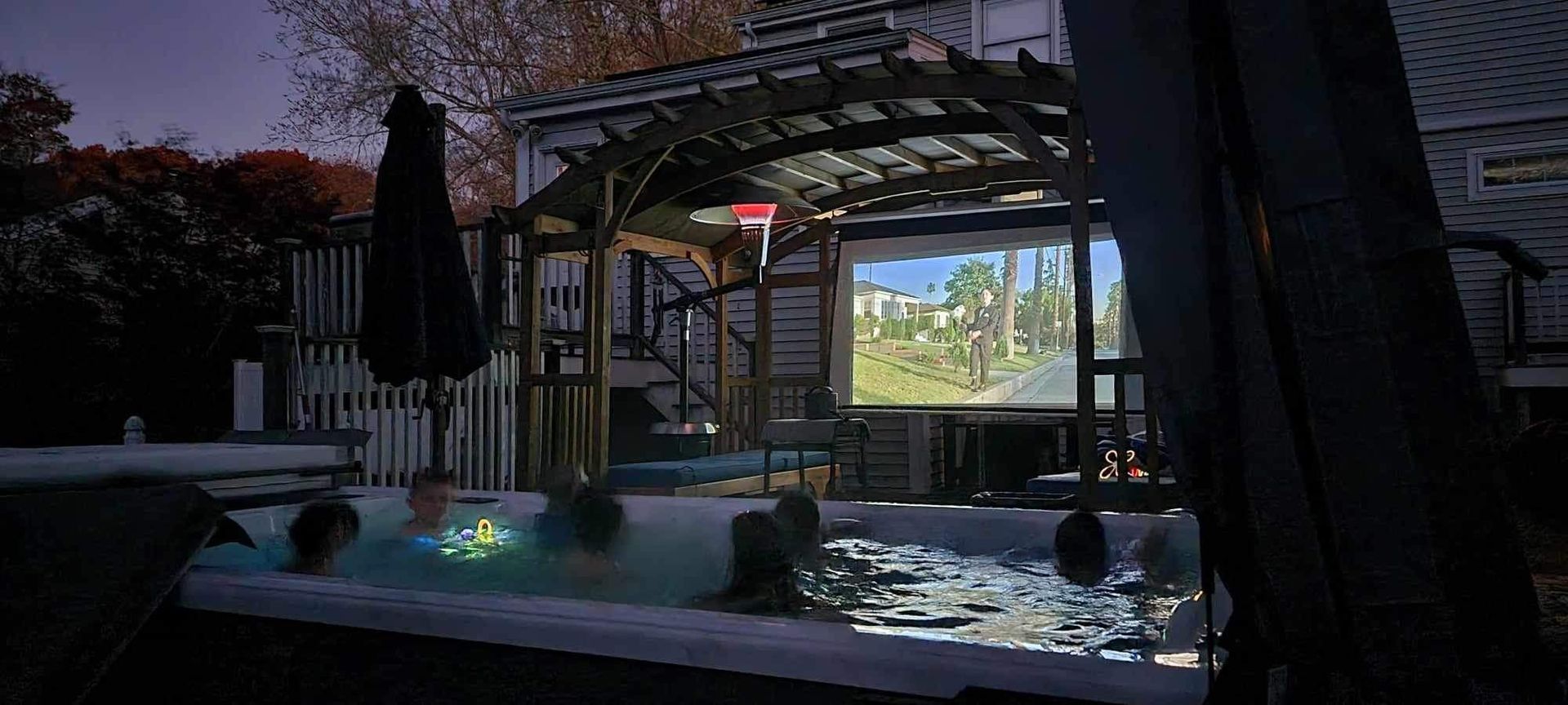 People watching a movie on a screen while in a hot tub outdoors at dusk.
