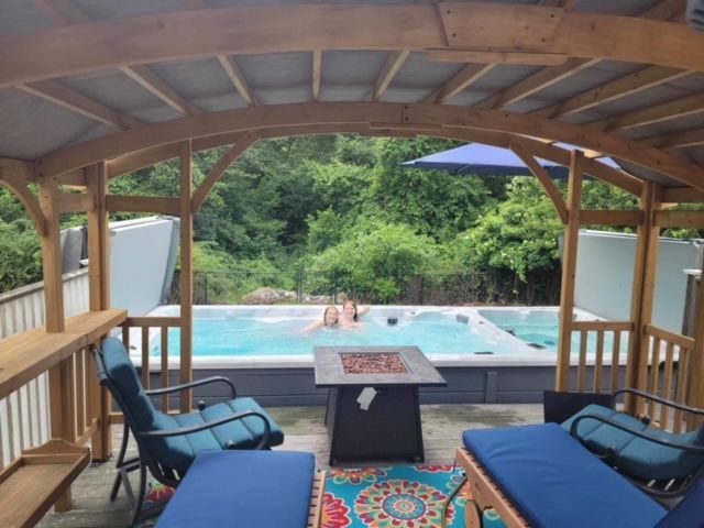 Relaxing outdoor spa area with pool, fire pit, and loungers under a wooden canopy.