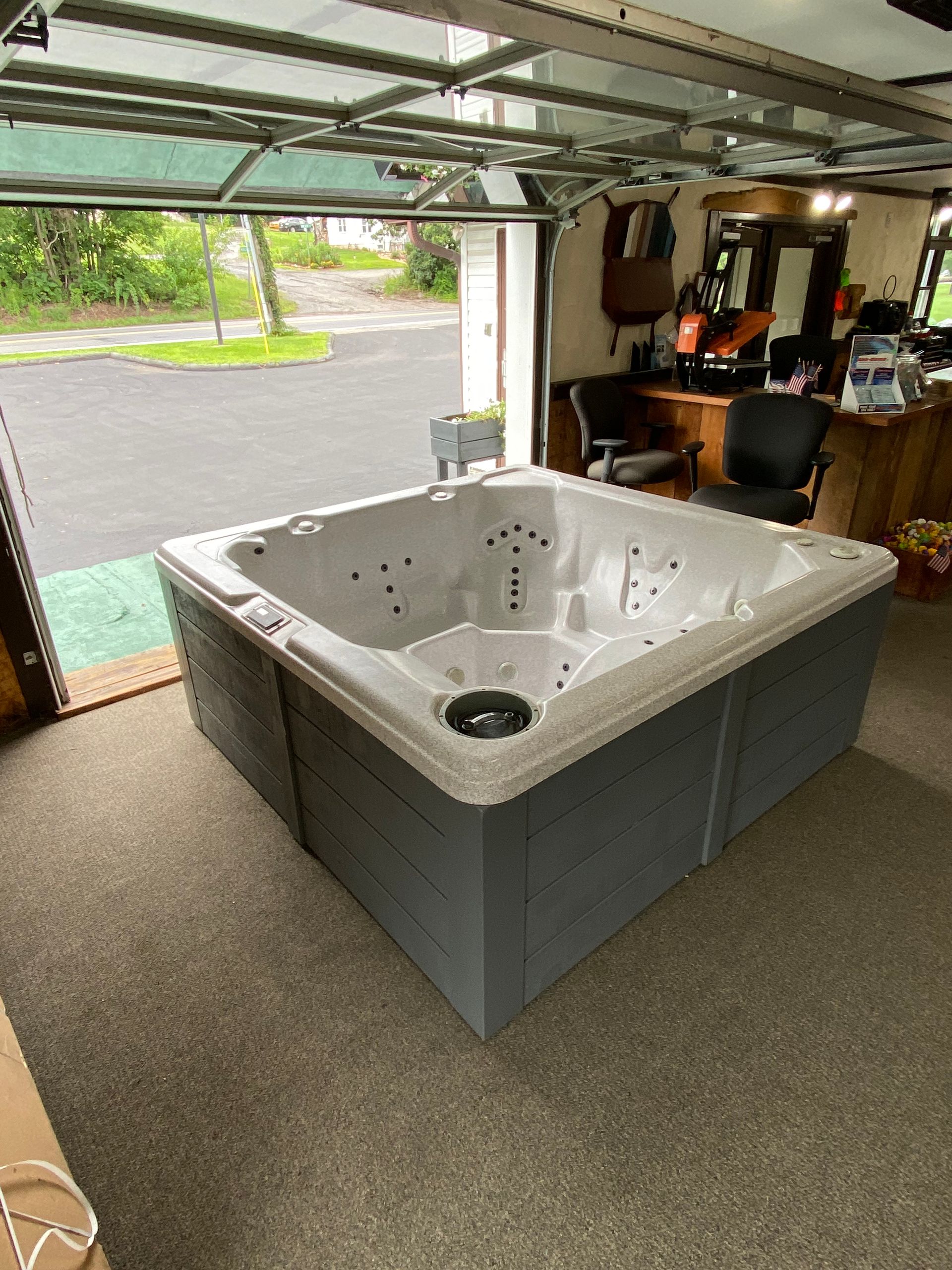 Hot tub with light brown wood paneling sits inside a garage with glass door.