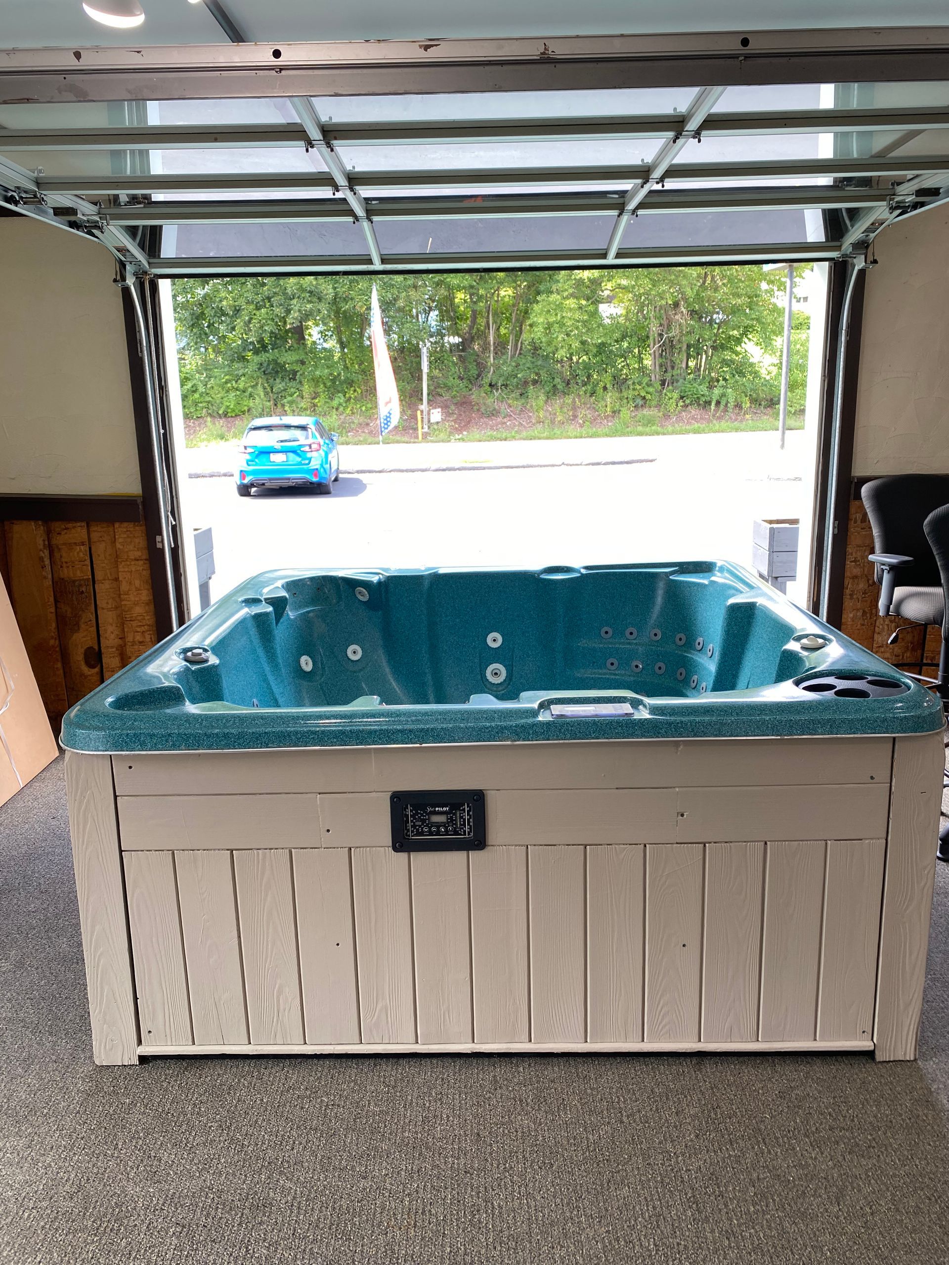Hot tub with light brown wood paneling sits inside a garage with glass door.