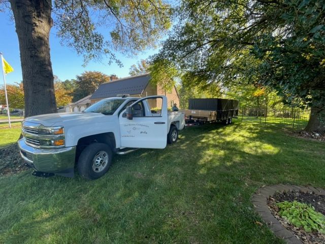 White pickup truck with trailer parked on grass, near a house and trees.